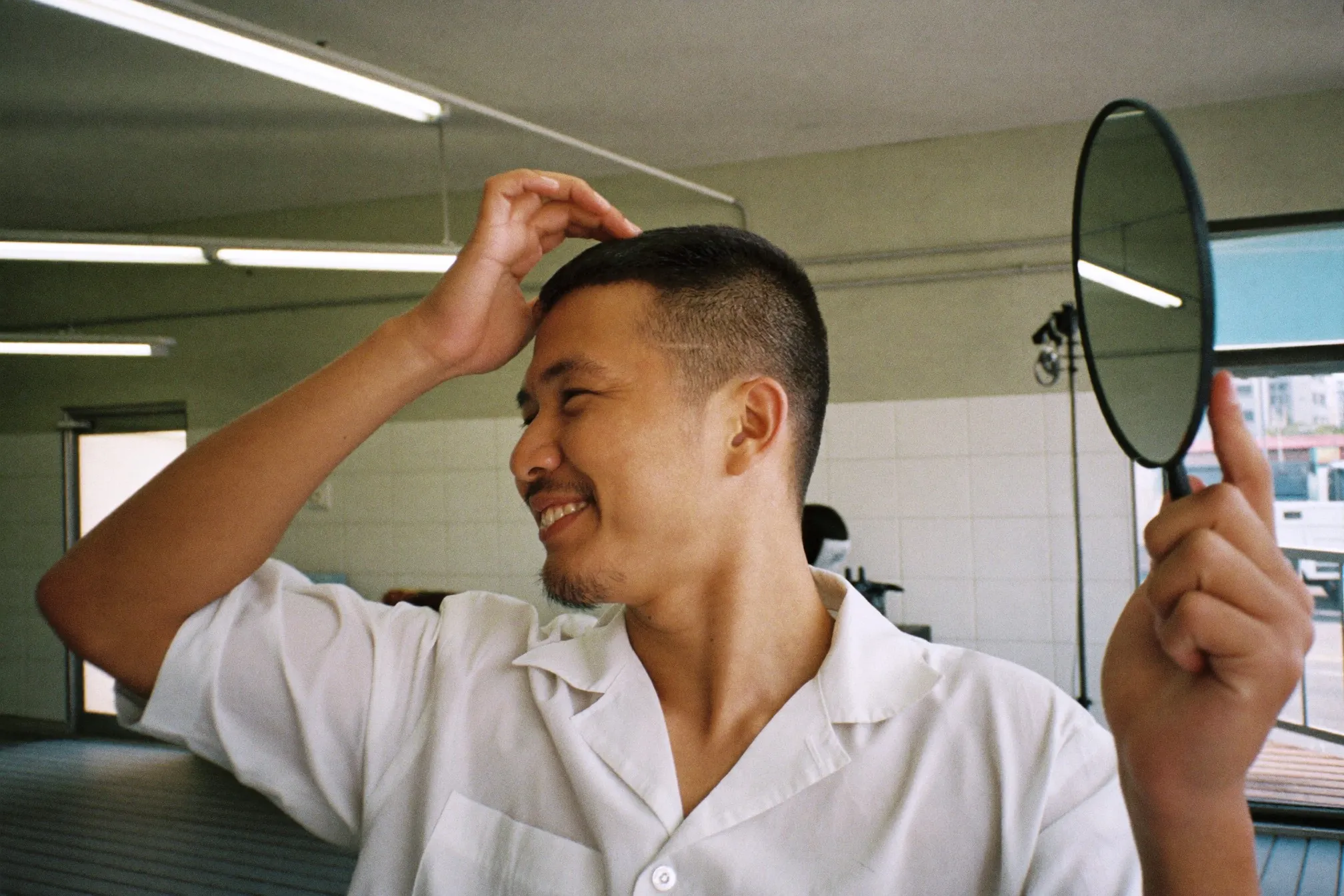 Man checking his fresh mid fade in a handheld mirror at a Singapore neighbourhood barbershop