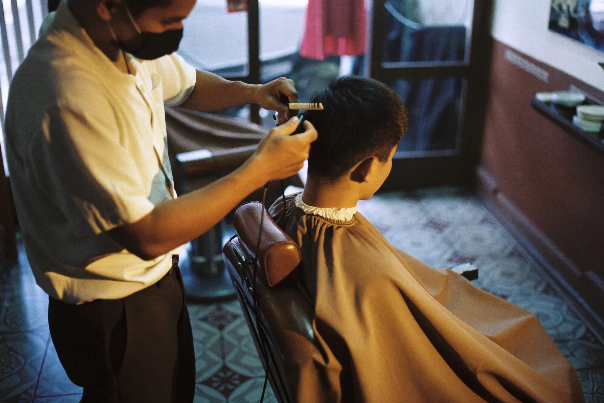 Barber shaping a low fade with clippers on a man seated in a Kuala Lumpur barbershop chair