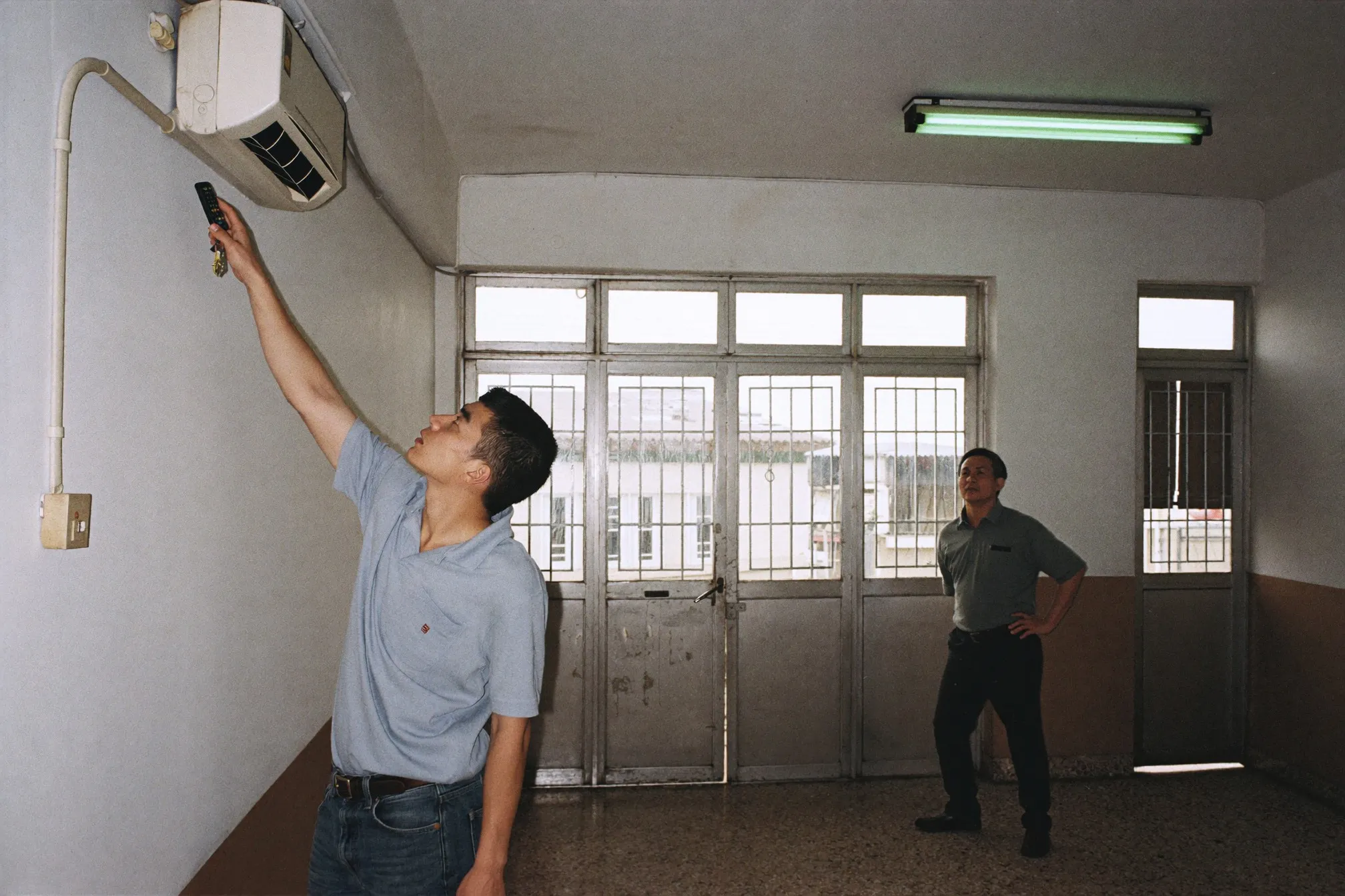 Man testing the air conditioner during an apartment viewing in an older Kuala Lumpur walk-up while the landlord waits