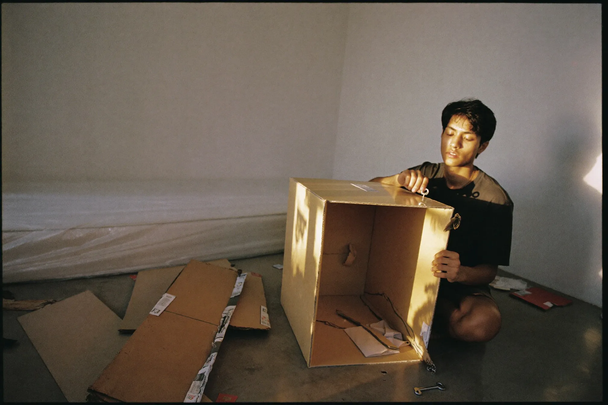 Man assembling a flat-pack wardrobe on the floor of a bare apartment bedroom surrounded by cardboard