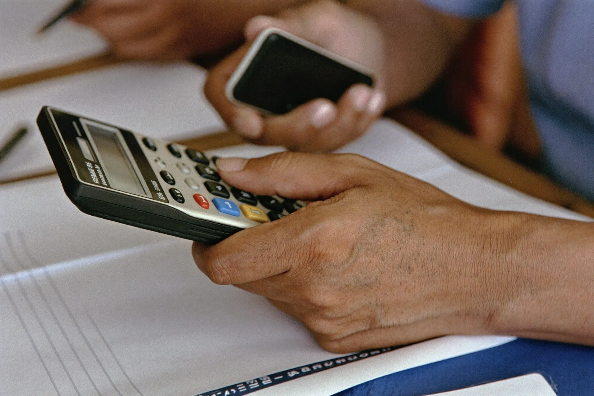Close view of a man's hands using a phone calculator over paperwork at a table