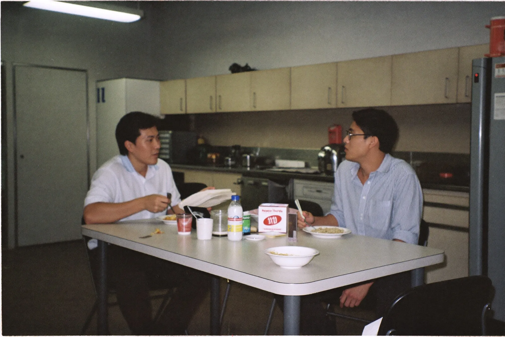 Two young colleagues talking over lunch at an office pantry table