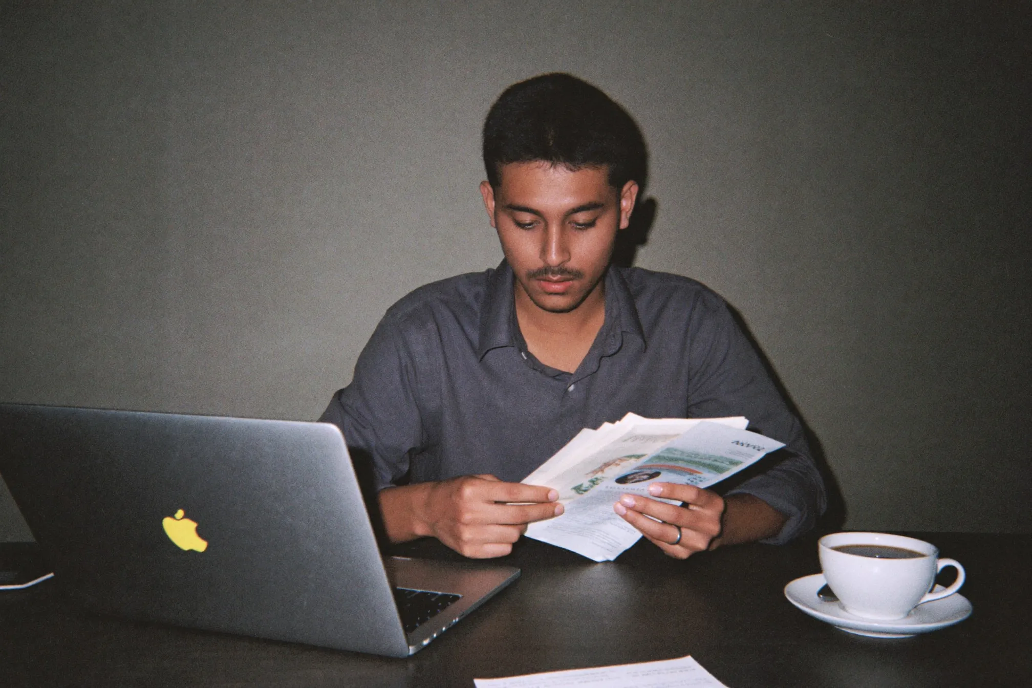 Young man at a desk reviewing his payslip beside a laptop and a cup of coffee