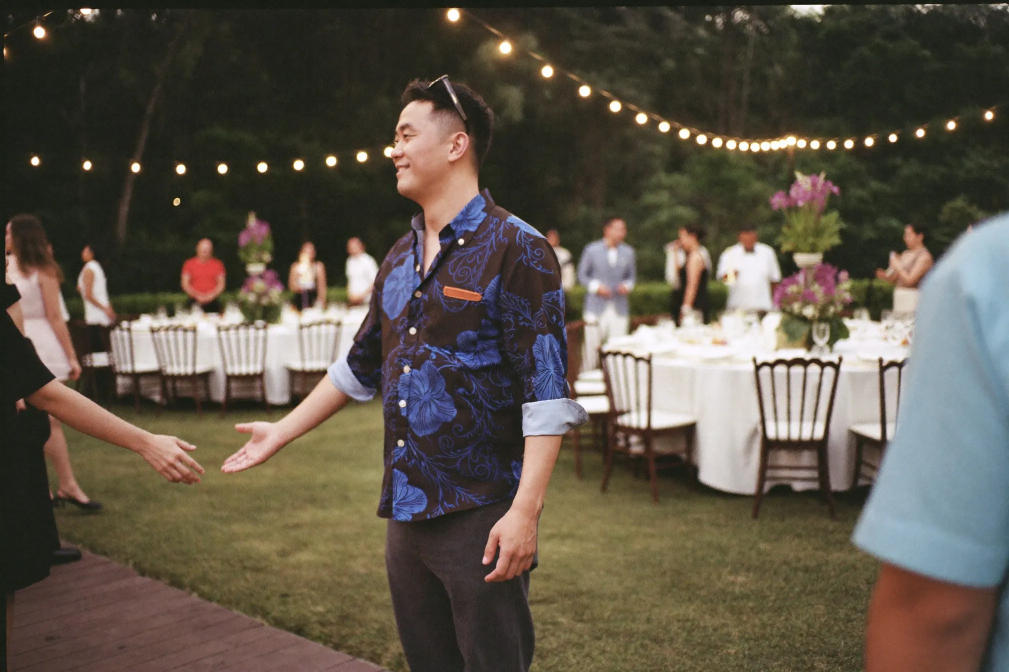 Man in a long-sleeved batik shirt and dark trousers greeting guests at an evening function