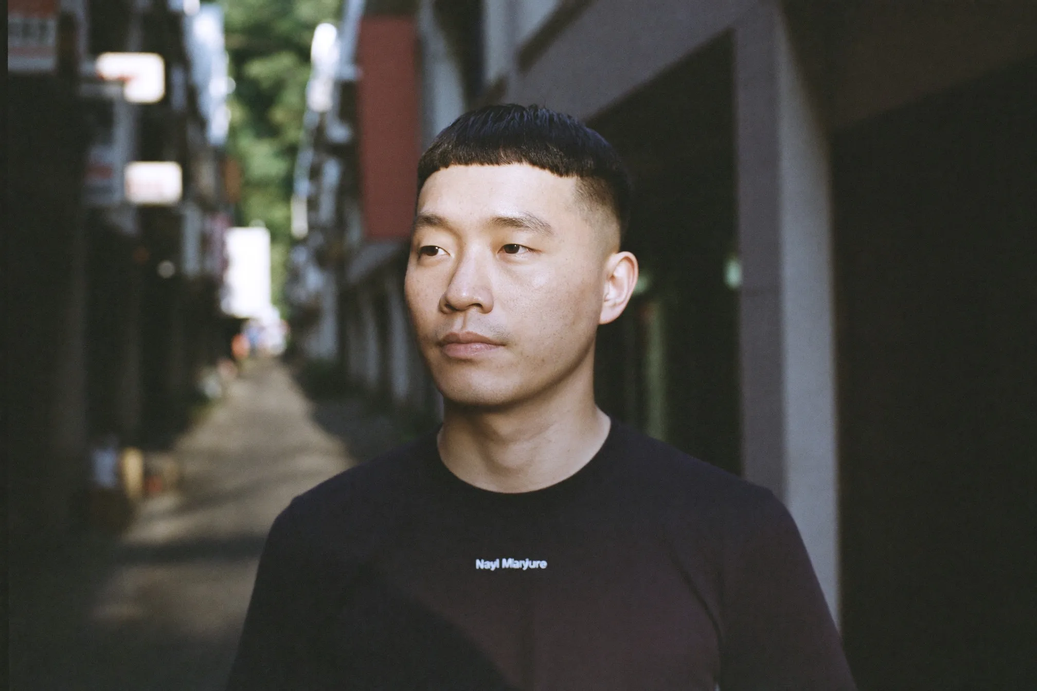 Chinese Malaysian man in his late twenties with a freshly cut French crop and blunt forward fringe standing on a shophouse street in Kuala Lumpur