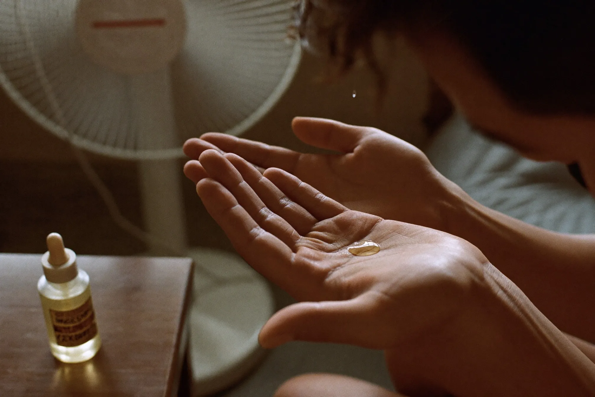 Close view of a man's hands rubbing a few drops of hair oil between his palms beside a standing fan