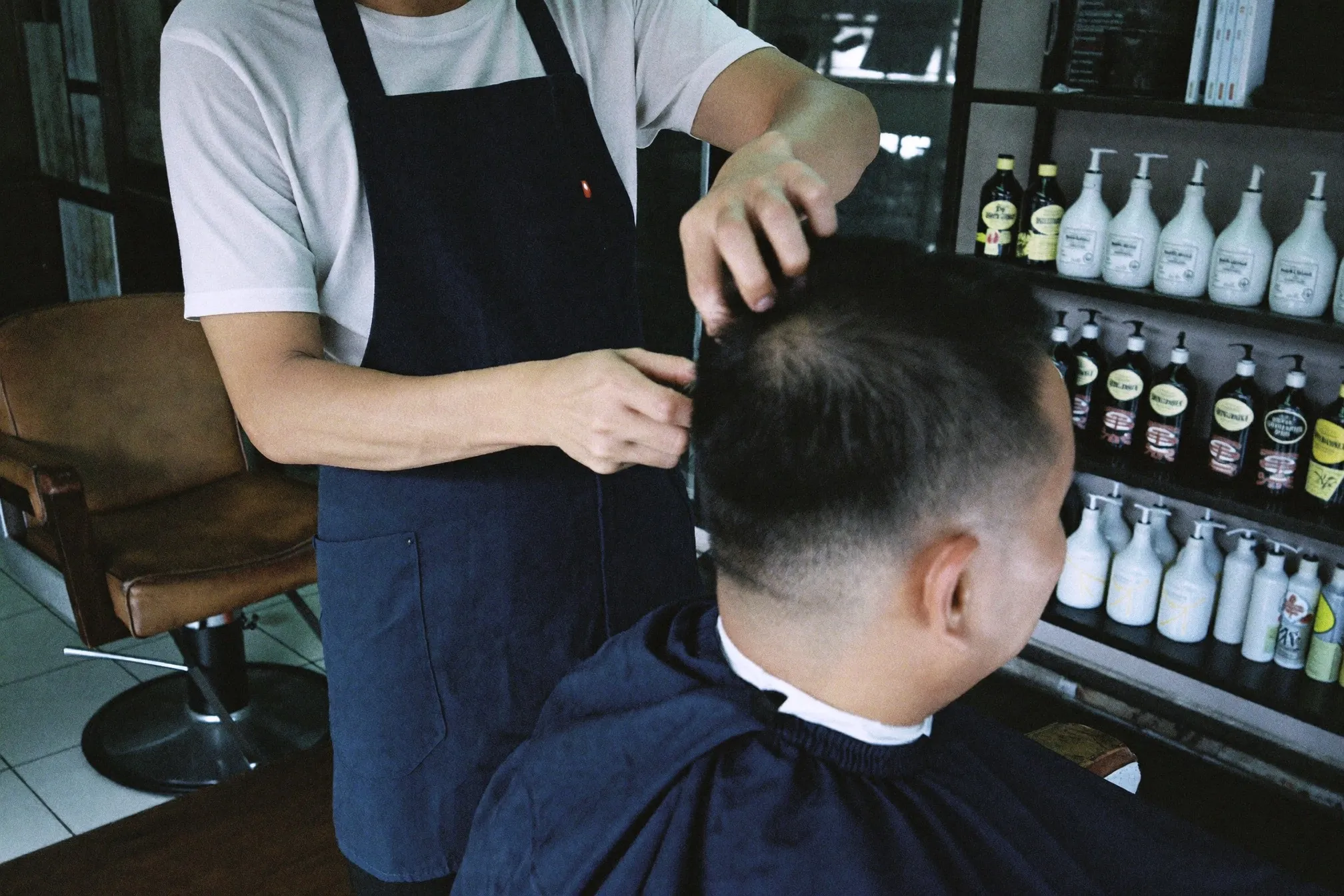 Barber point-cutting the ends of a Chinese Singaporean man's hair in a small neighbourhood barbershop