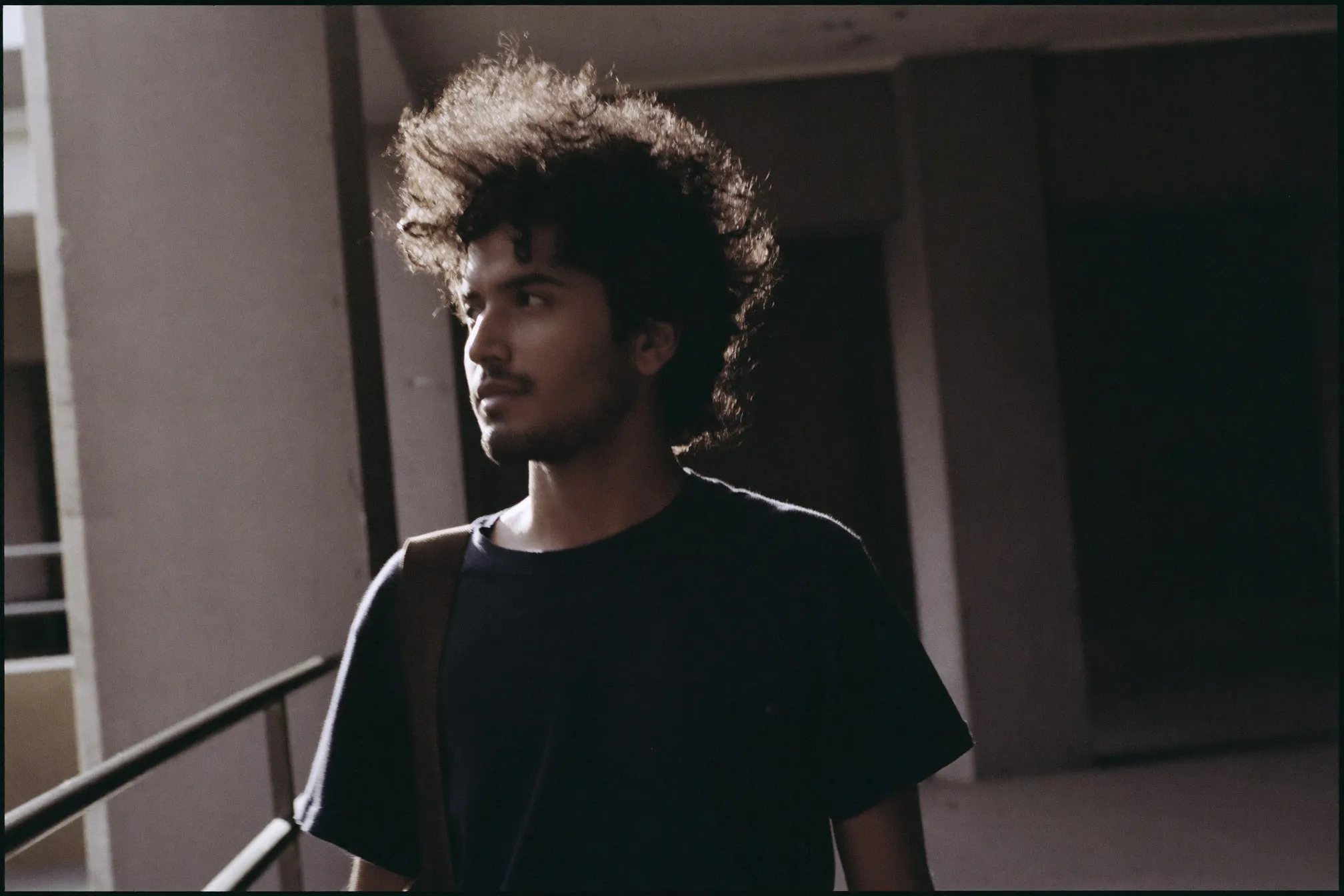 Indian Malaysian man with frizzy dark hair backlit by afternoon sun on a sheltered walkway in Kuala Lumpur
