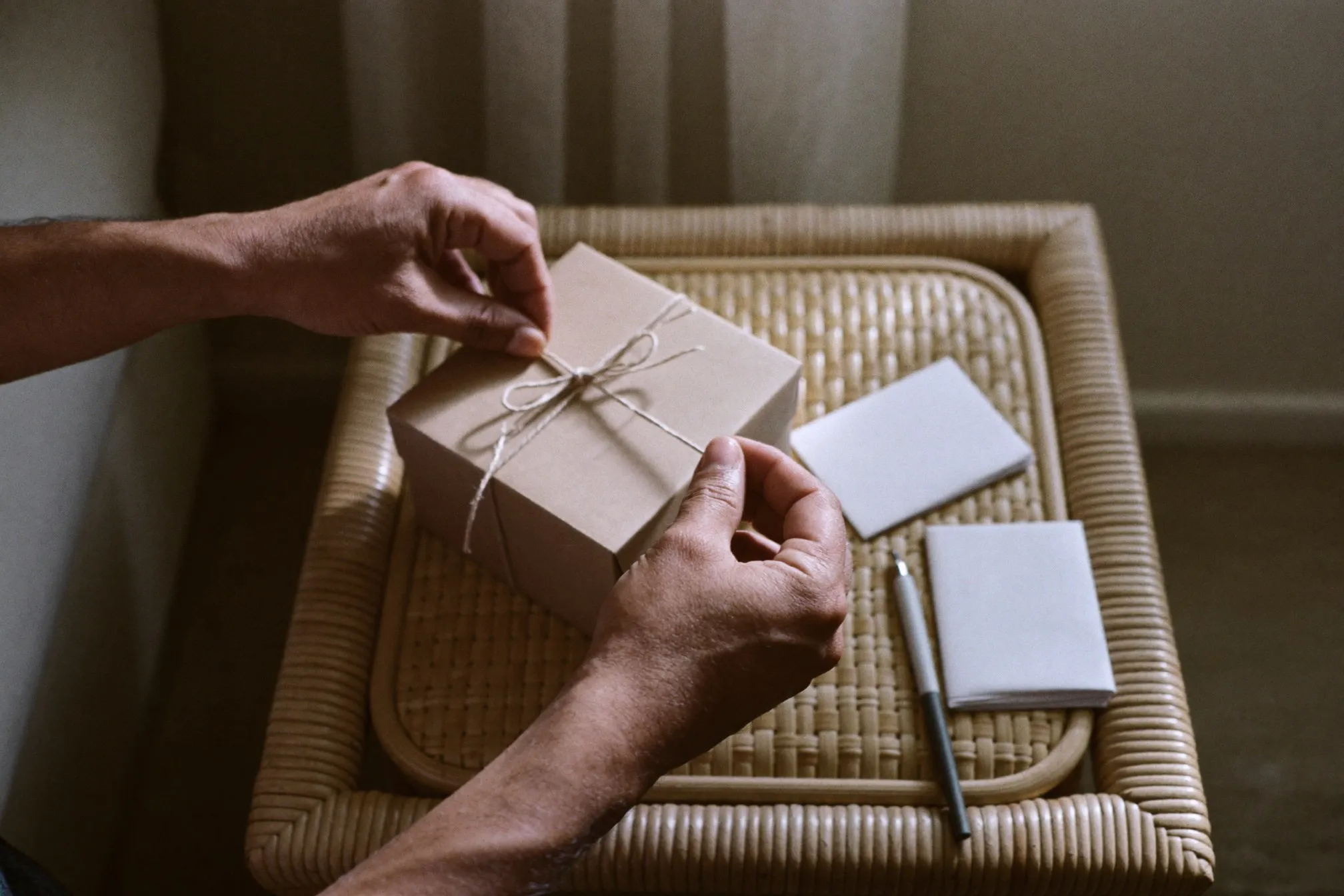 Hands tying twine around a plain wrapped gift box on a rattan table in a Singapore flat
