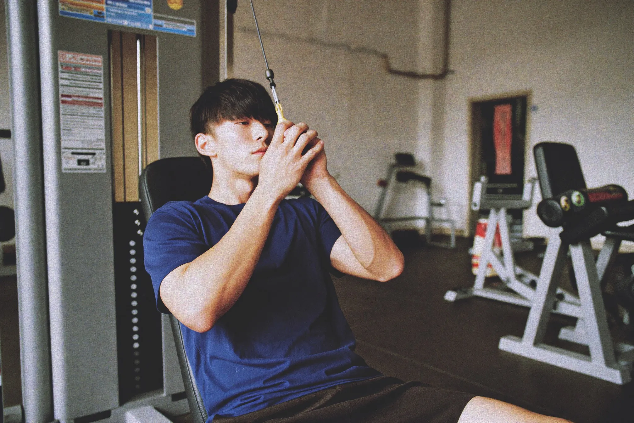 Chinese Singaporean man adjusting the seat of a chest press machine in a quiet gym