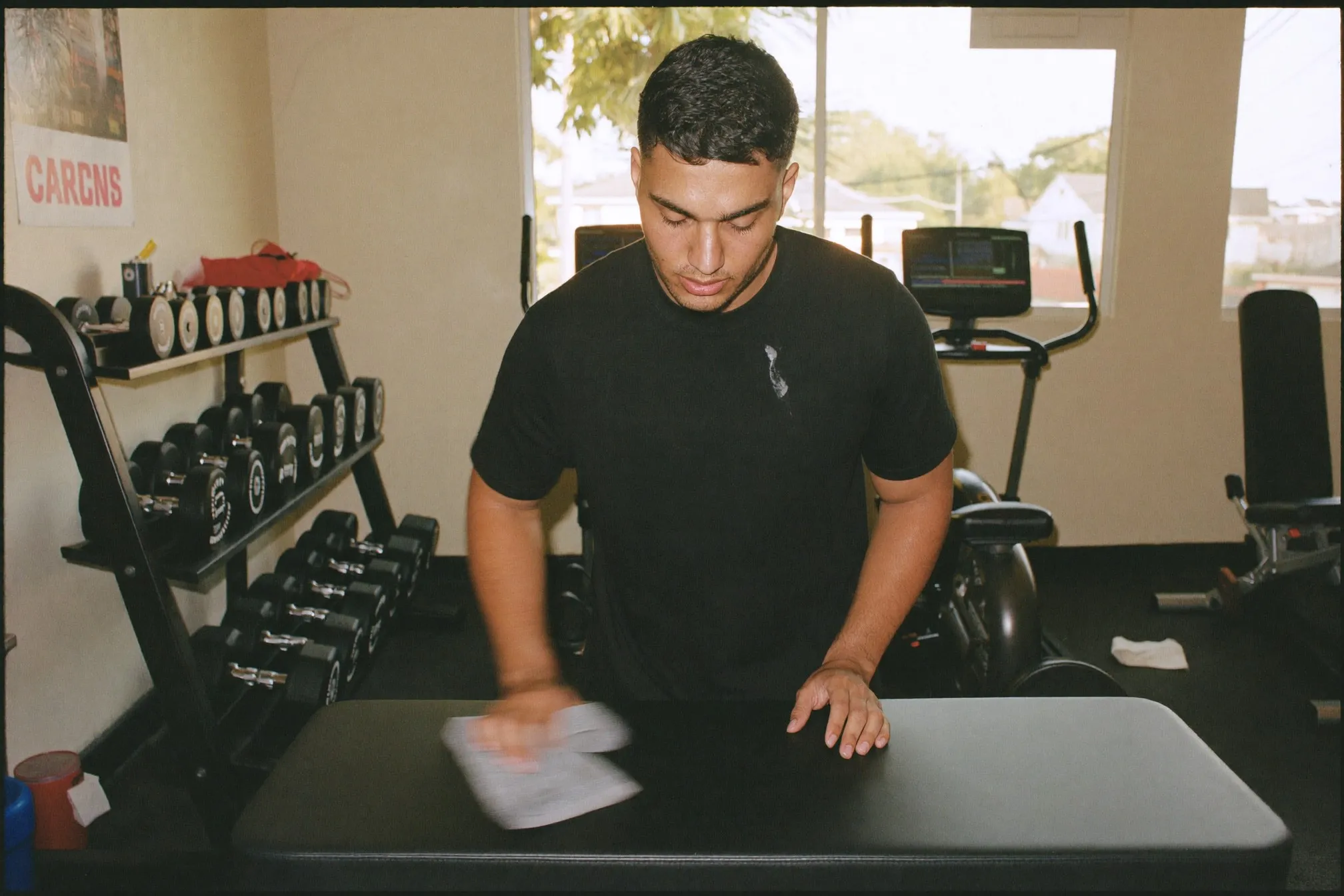 Indian man wiping down a workout bench with a towel in a neighbourhood gym in the evening