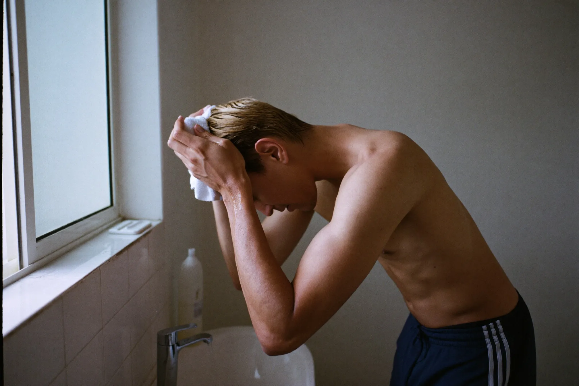 Man towel-drying freshly washed lightened hair at a bathroom sink