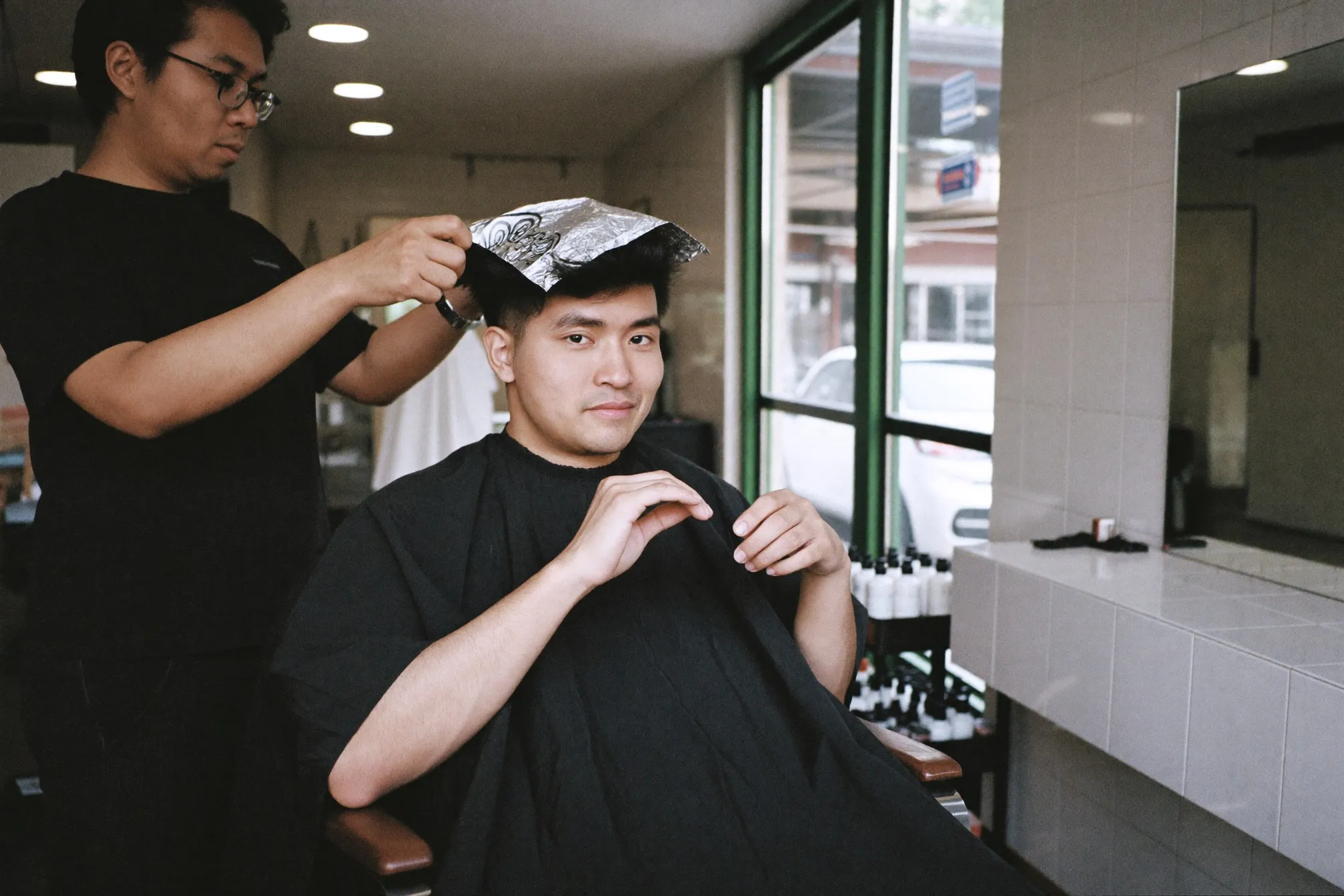 Stylist folding foils into a young man's dark hair in a small salon chair
