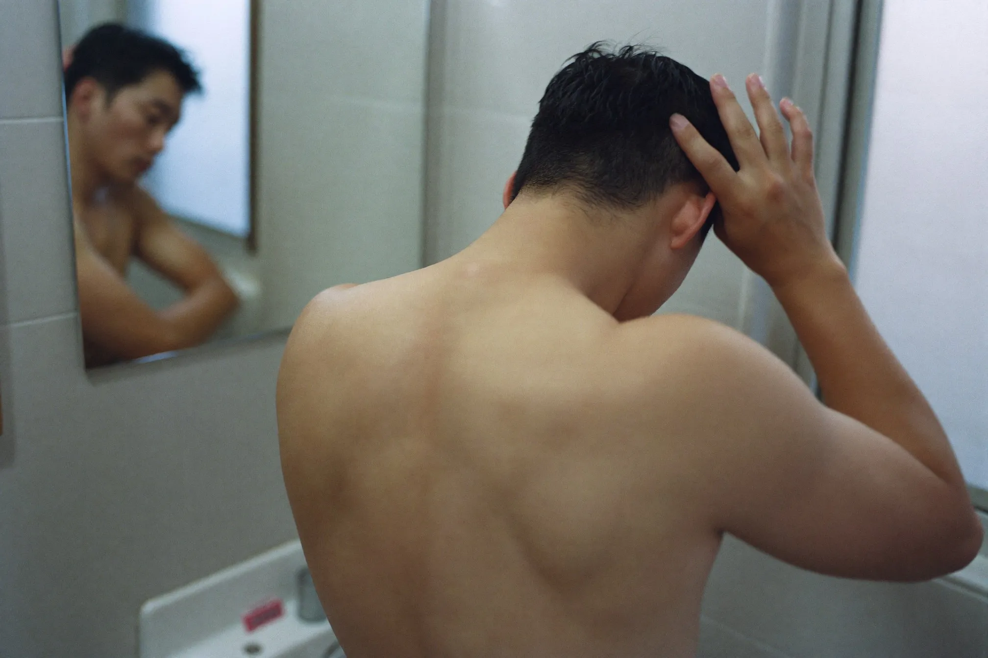 Man parting his hair with his fingers in front of a bathroom mirror to check his hairline