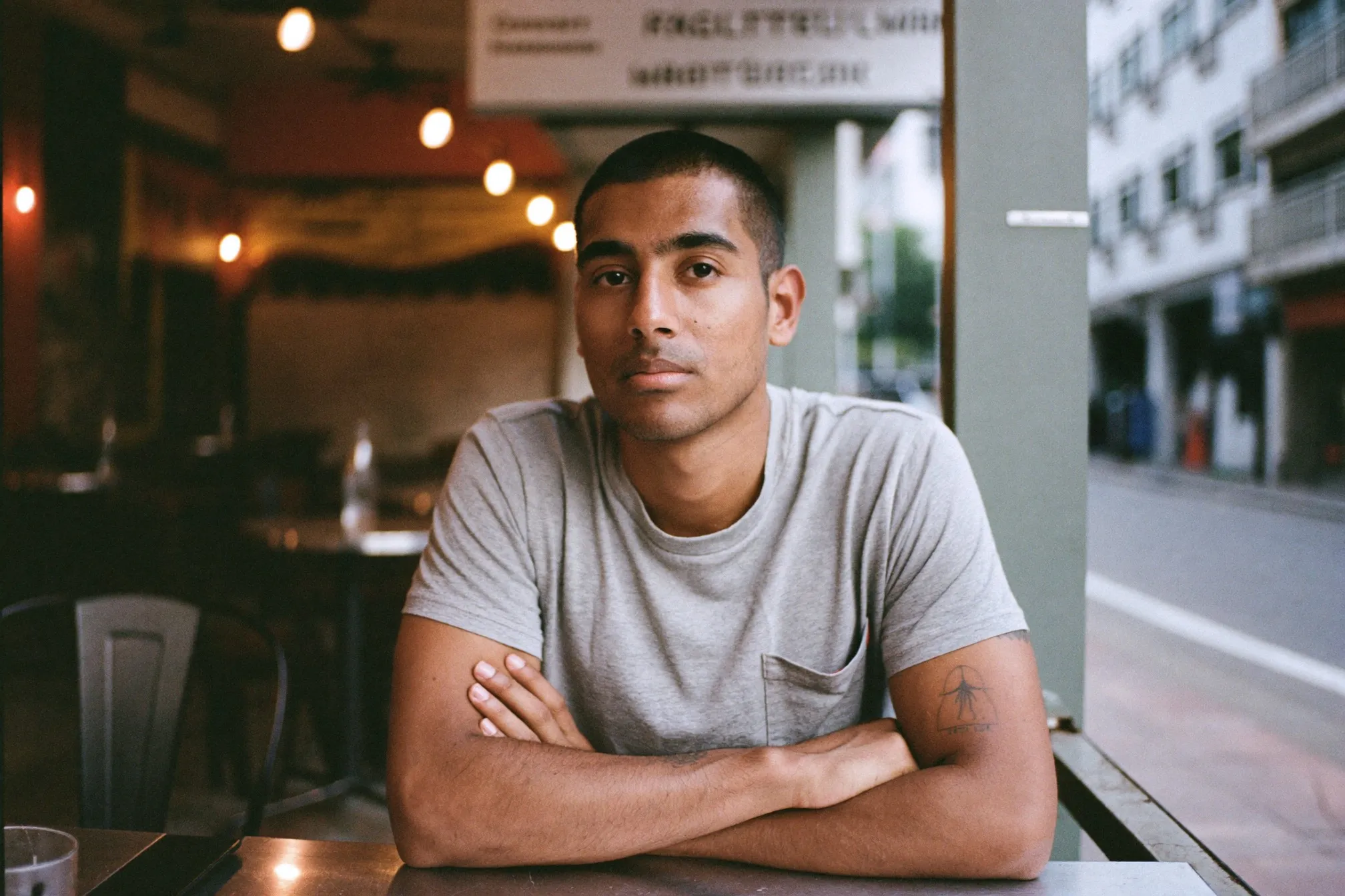 Man with a closely buzzed haircut sitting at an outdoor kopitiam table in the evening