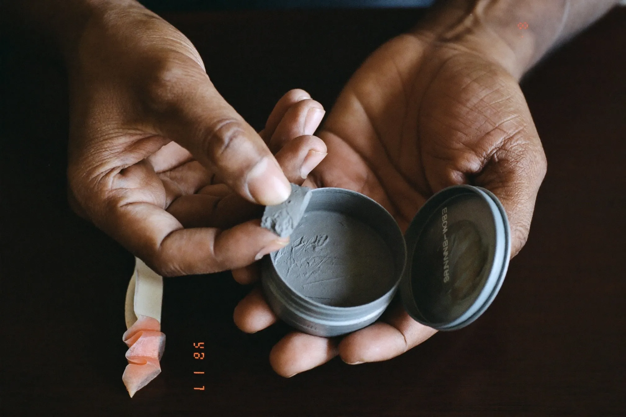 Close view of a man scooping clay from an open unbranded tin, product visible on his fingertips