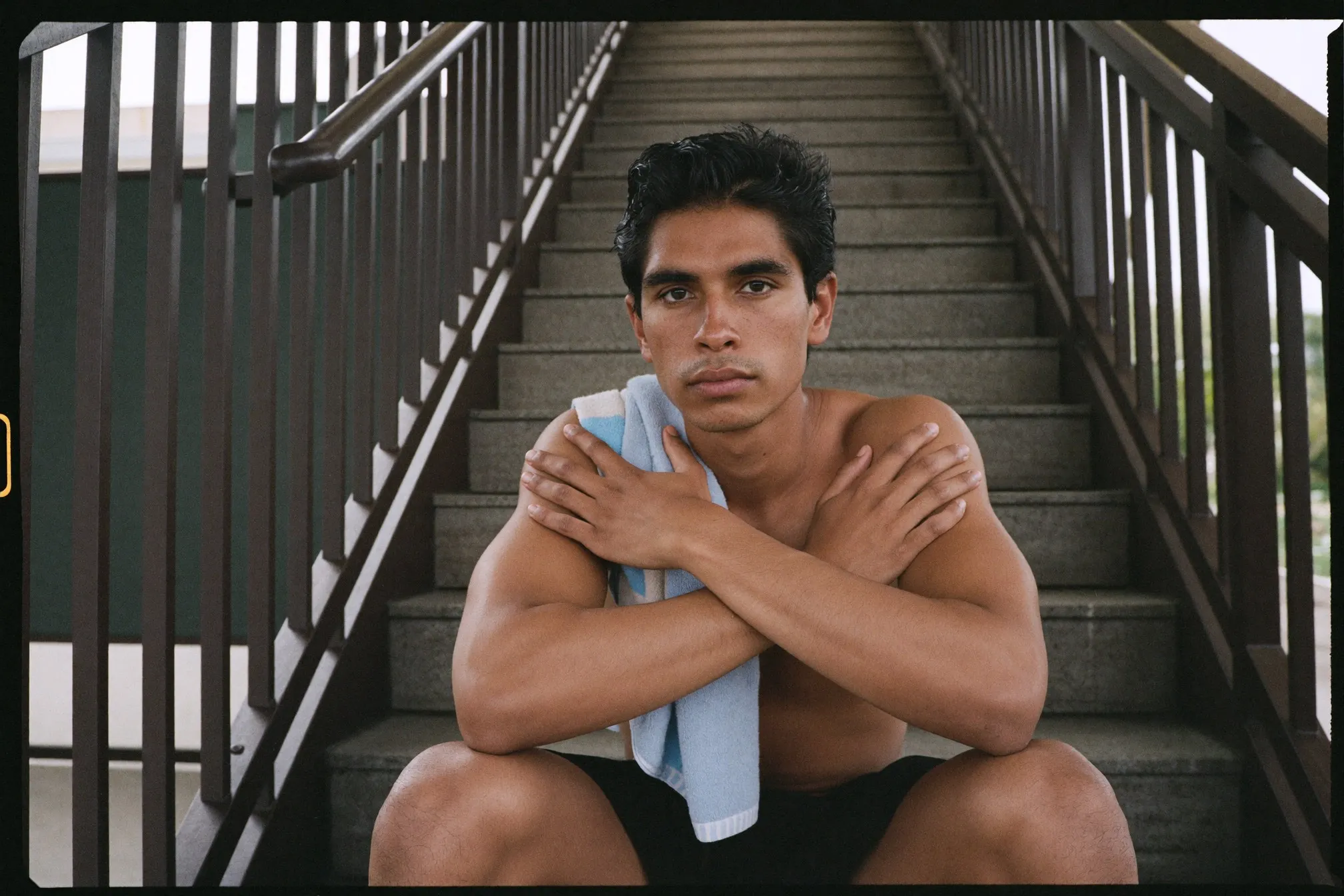Indian Malaysian man resting with hands on knees and a towel over his shoulder on a stairwell landing after a workout