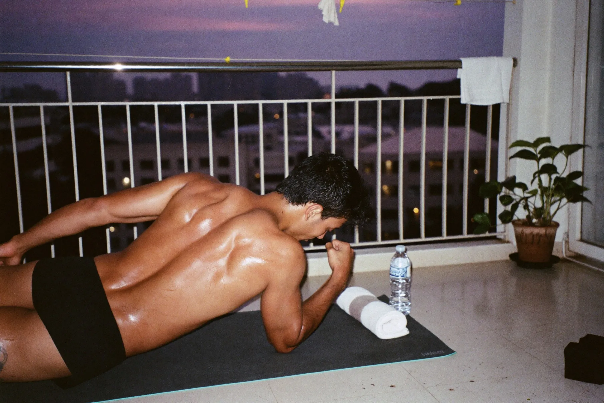 Indian man holding a plank on a mat on a condominium balcony in Petaling Jaya at dusk