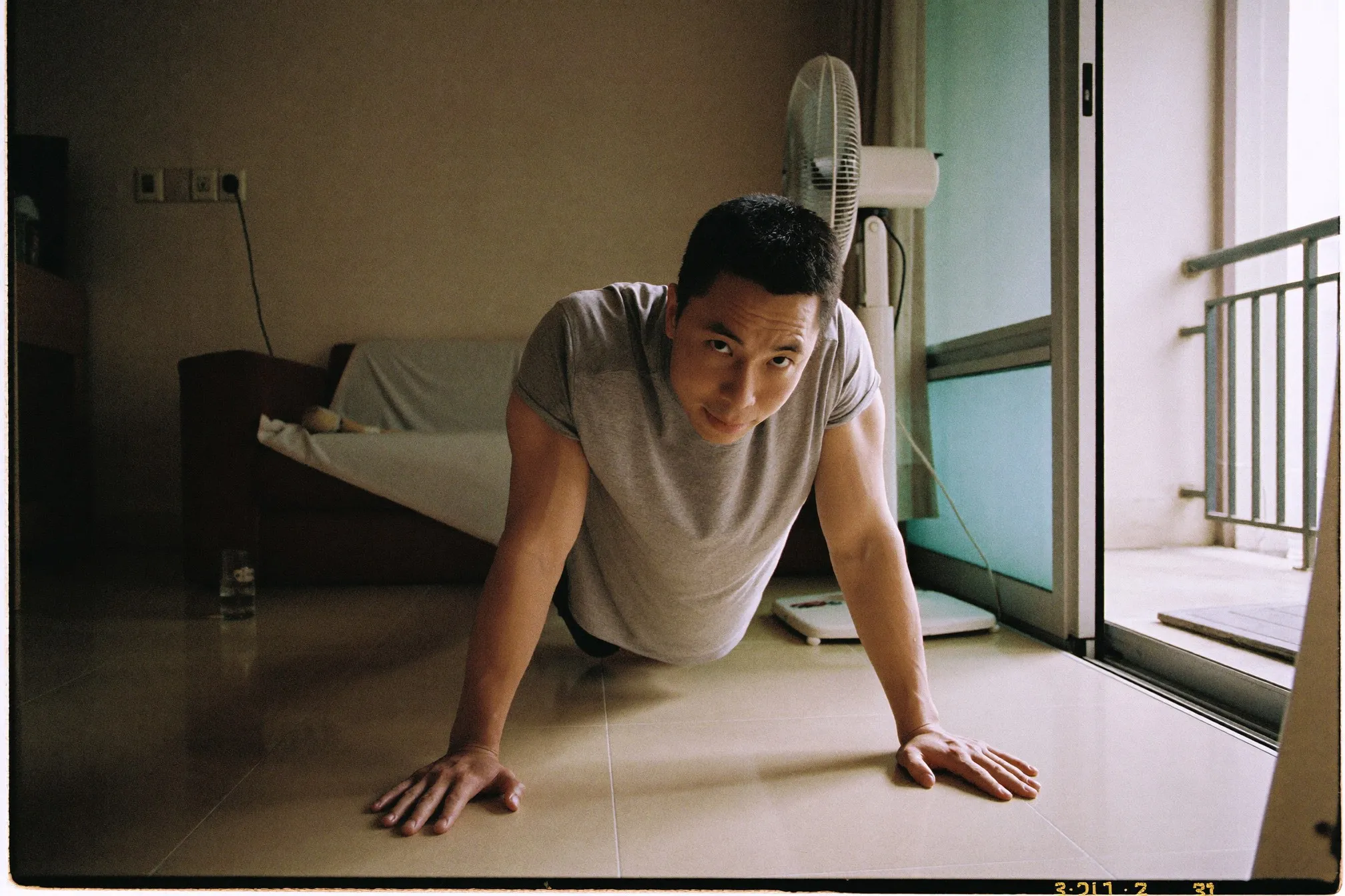 Chinese Malaysian man doing push-ups on the tiled floor of a small Kuala Lumpur apartment living room in early morning light