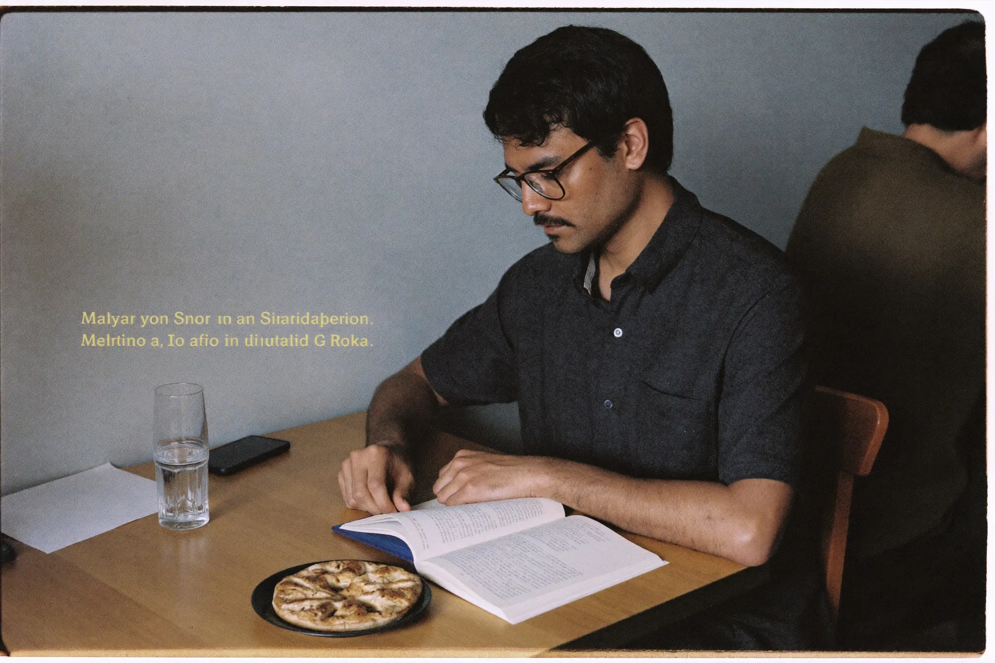 Man reading a book at a kopitiam table with a flat white, notebook open beside him