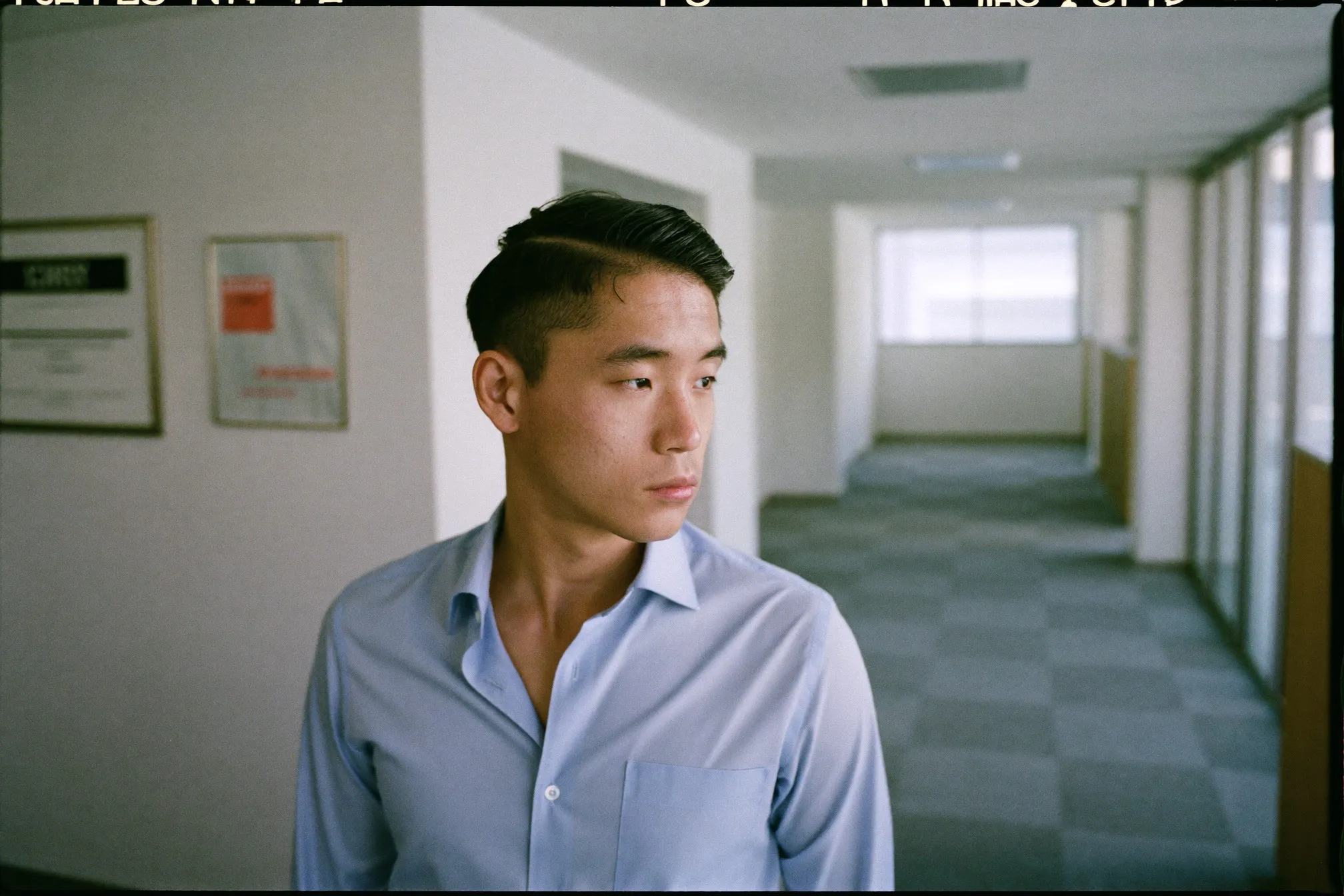 Chinese Singaporean man in his early thirties with a freshly cut ivy league haircut, front hair combed into a side part, standing in an office corridor