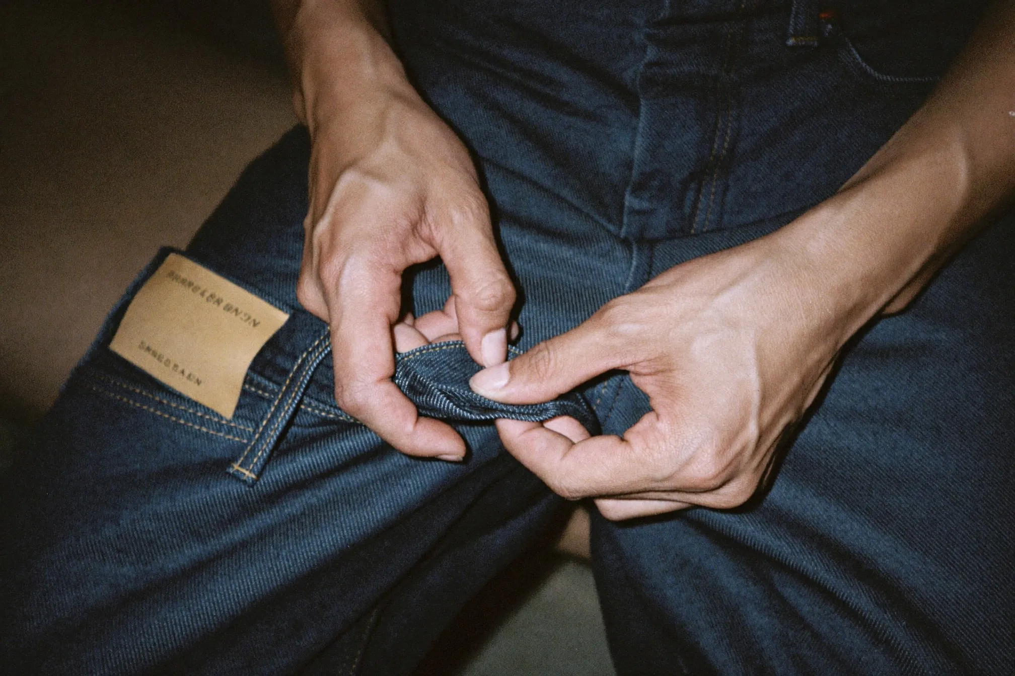 Close view of hands checking the hem and leg opening of a pair of dark indigo jeans