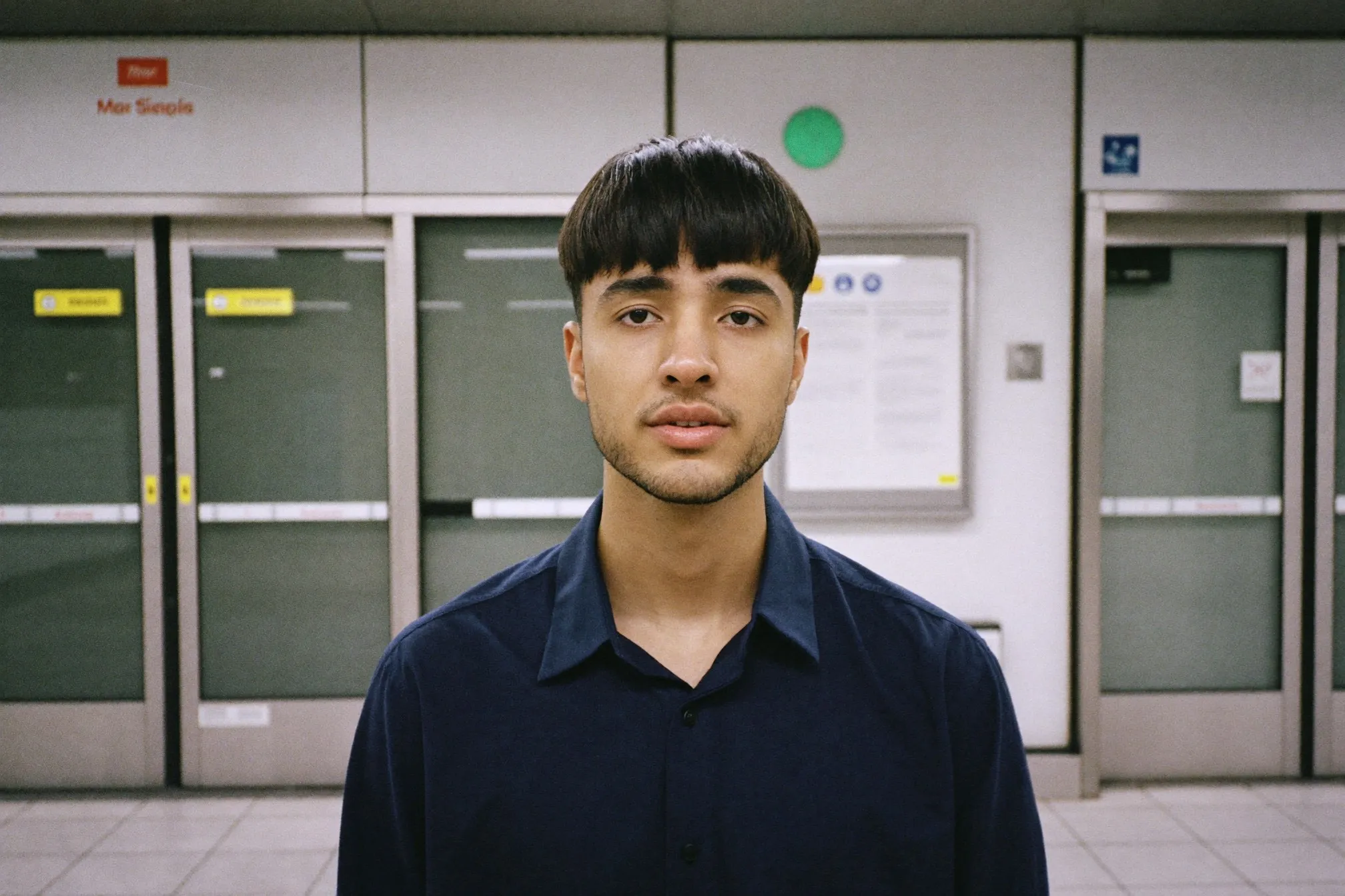 Young Indian man with a permed curtain fringe waiting on an MRT platform in Singapore