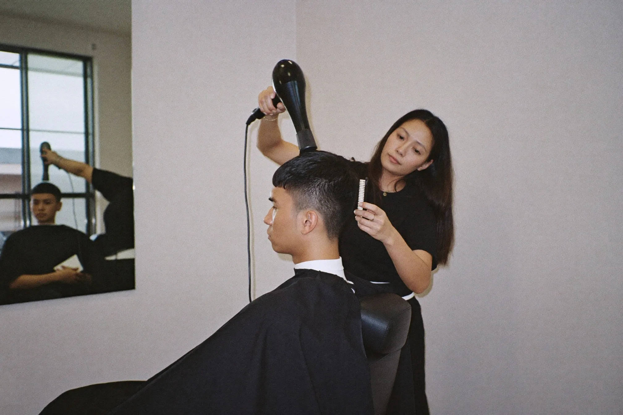 Stylist blow-drying the comma fringe of a young Chinese Malaysian man in a bright Korean-style hair salon in Kuala Lumpur
