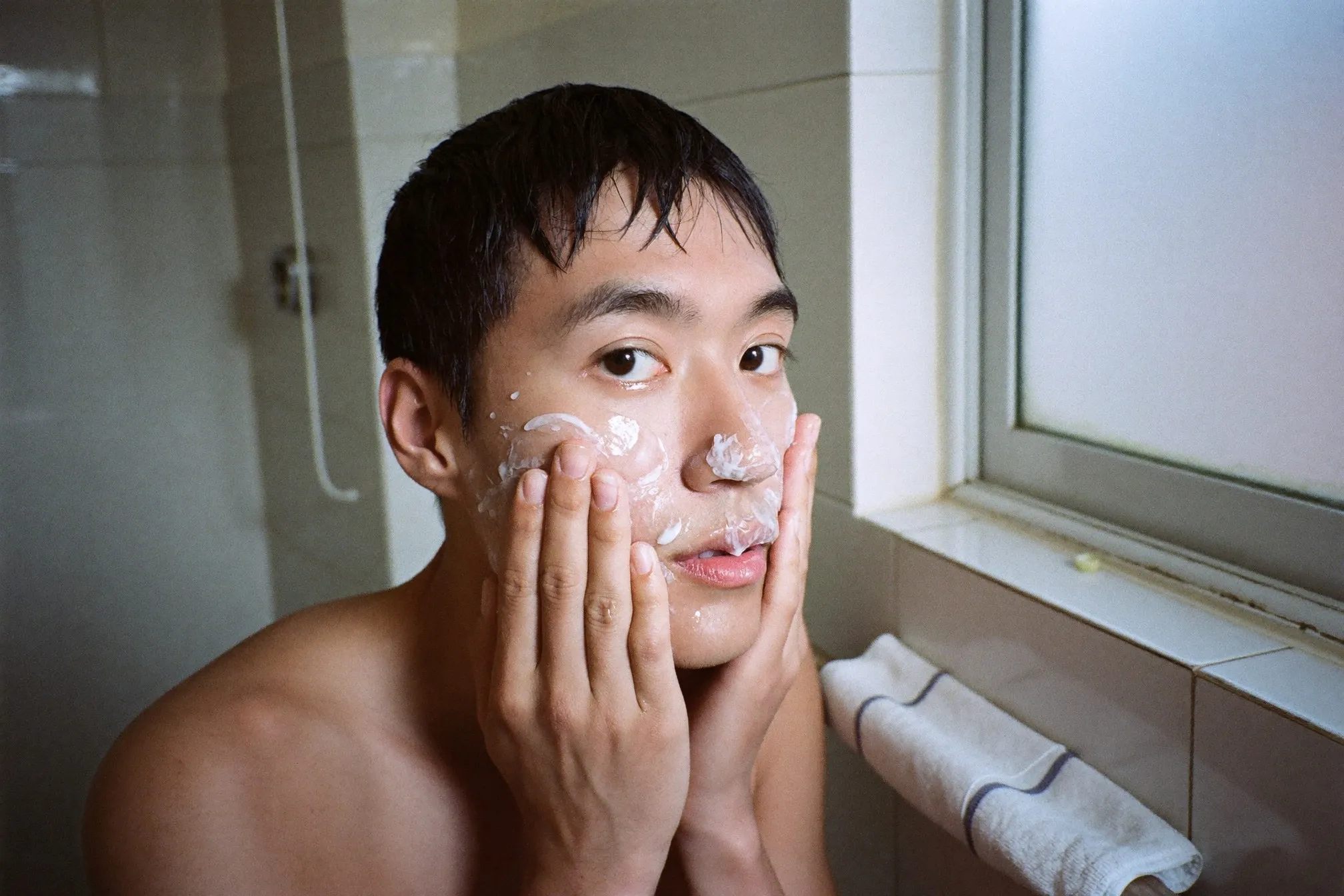 Man patting a watery lotion into his face in a small condo bathroom in the morning