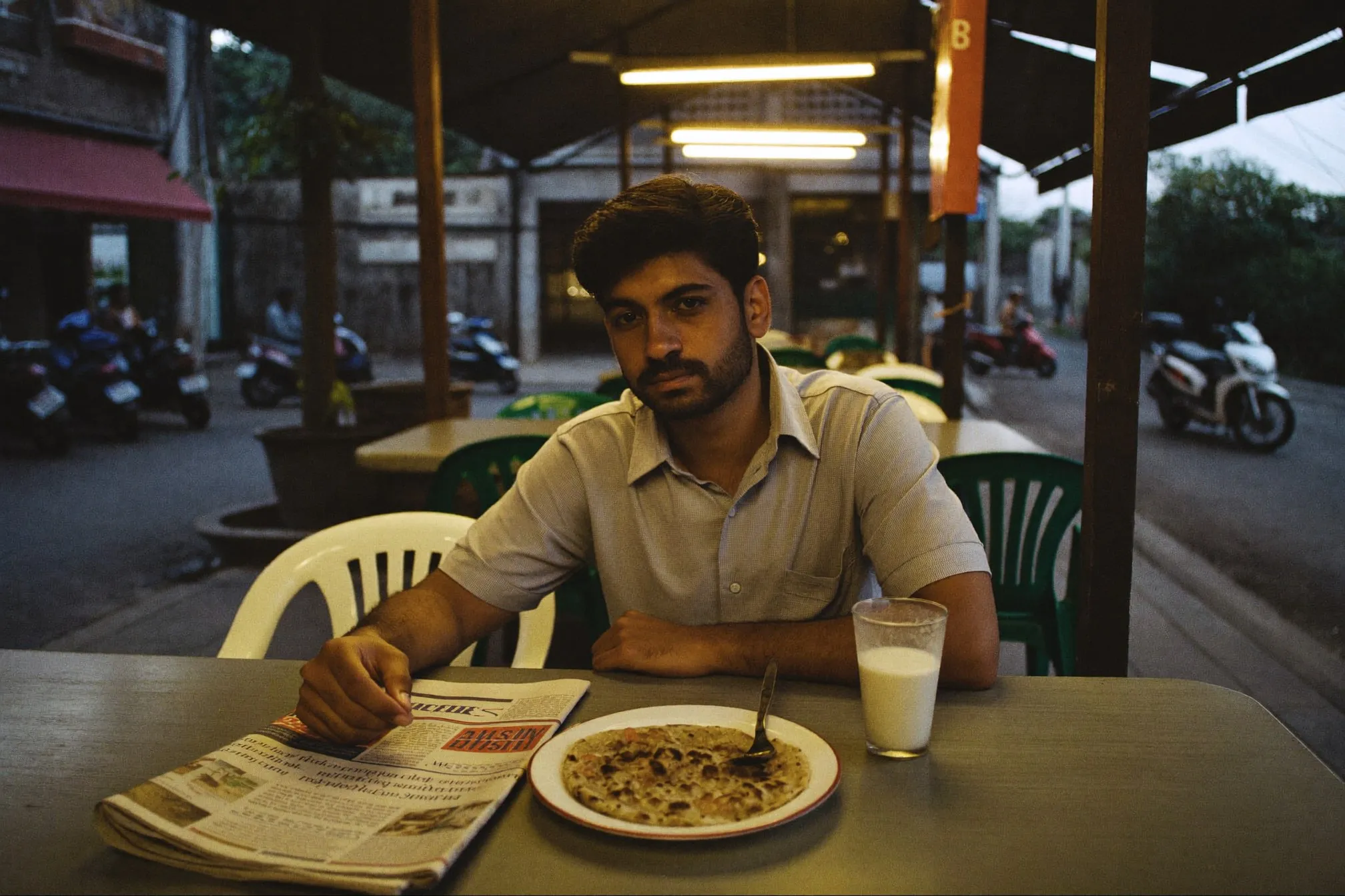 Man in his thirties sitting alone at a mamak table at night with a plate of roti canai and a glass of tea