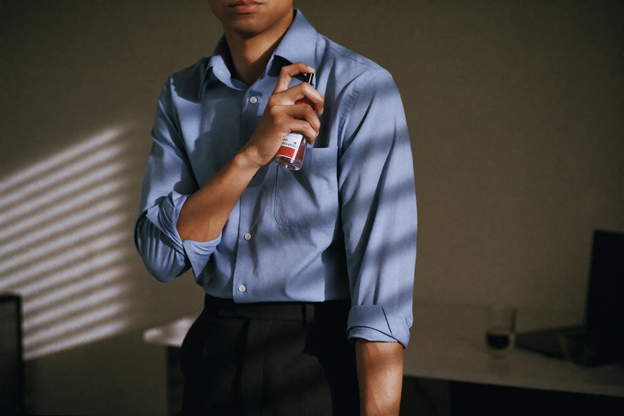 Man in office clothing topping up fragrance from a small travel atomiser at his desk in the afternoon