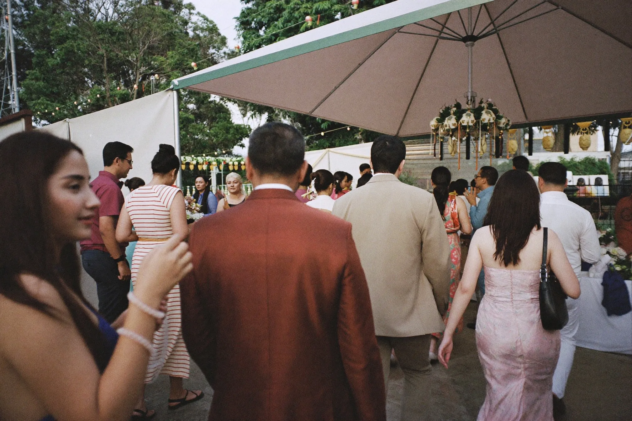 Guests arriving at a decorated outdoor Malay wedding kenduri under a canopy in the afternoon