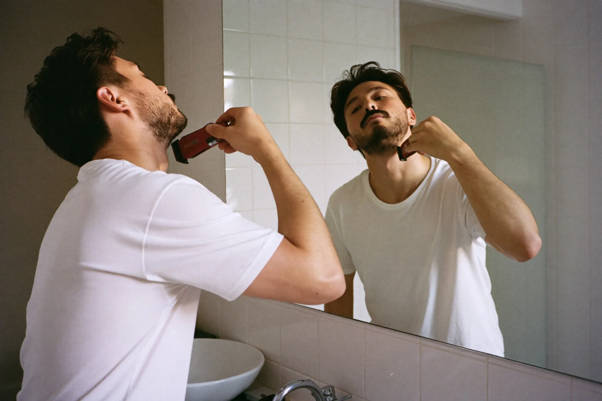 Man trimming his beard neckline in front of a bathroom mirror in the morning