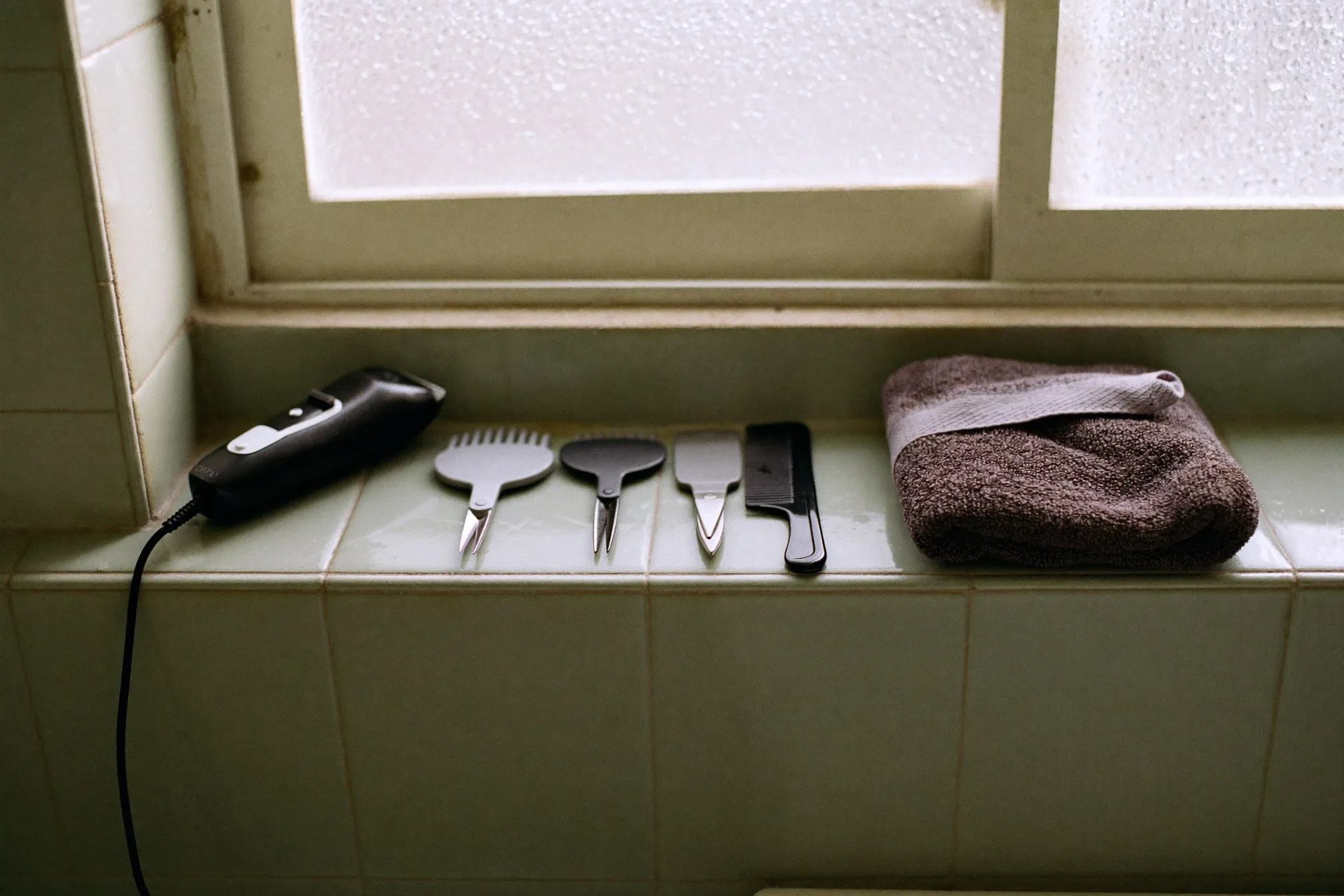 Grooming tools laid out on a bathroom shelf: an unbranded body trimmer with guards, small scissors and a comb beside a folded towel