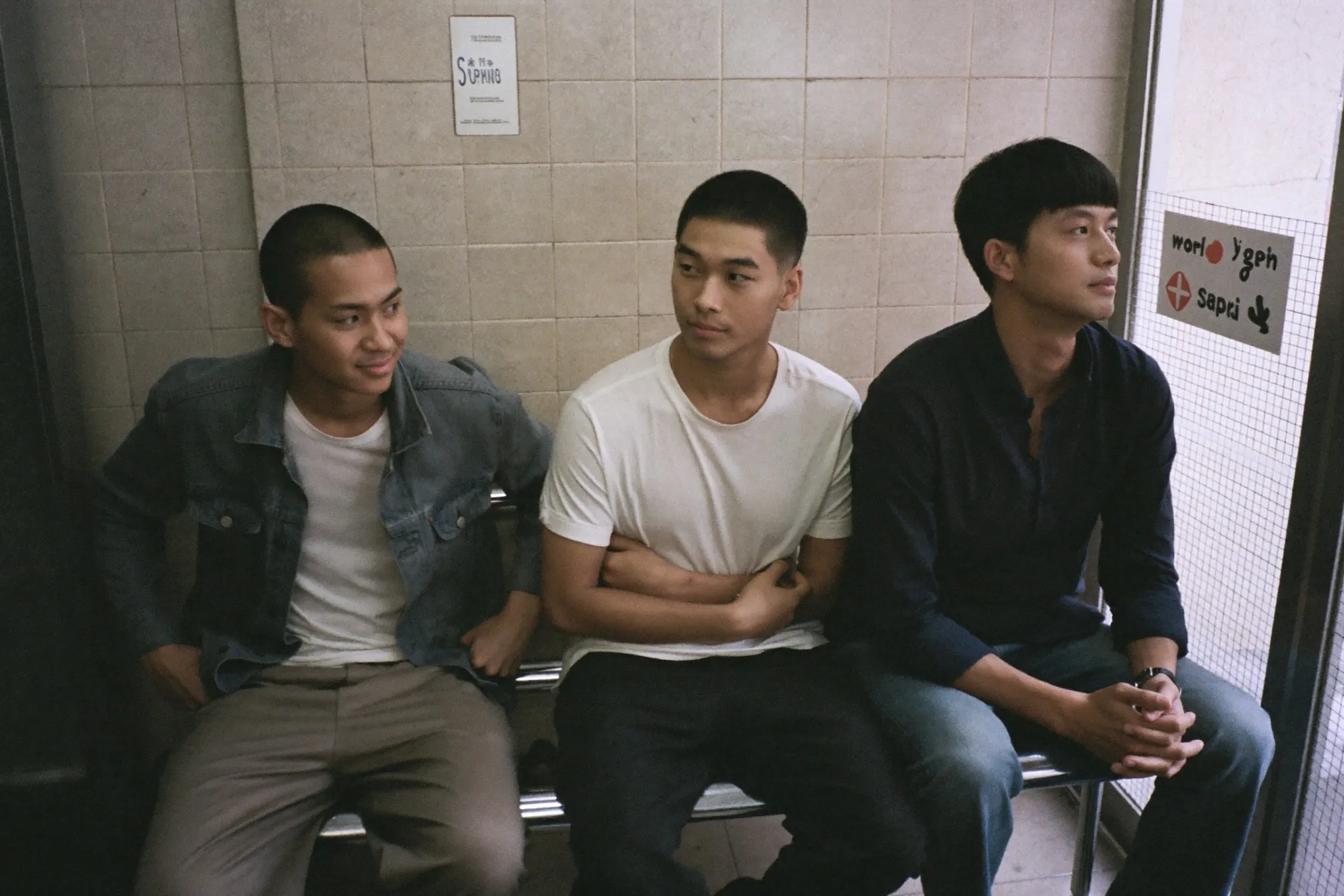 Three men waiting on a bench in a Singapore barbershop with a buzz cut, a textured crop and a two block haircut