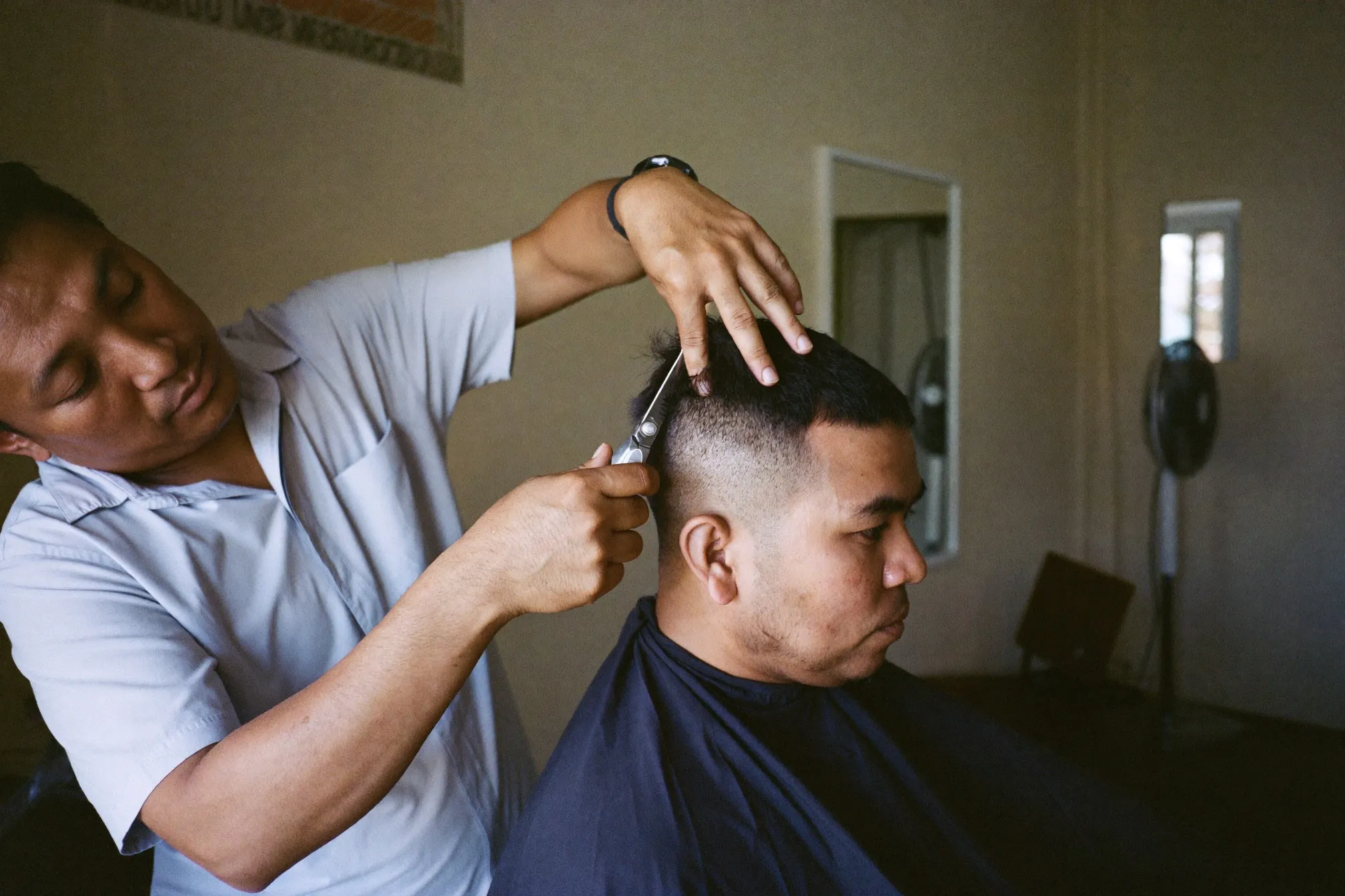 Barber scissor-cutting the top of a textured crop on a seated man in a Petaling Jaya barbershop