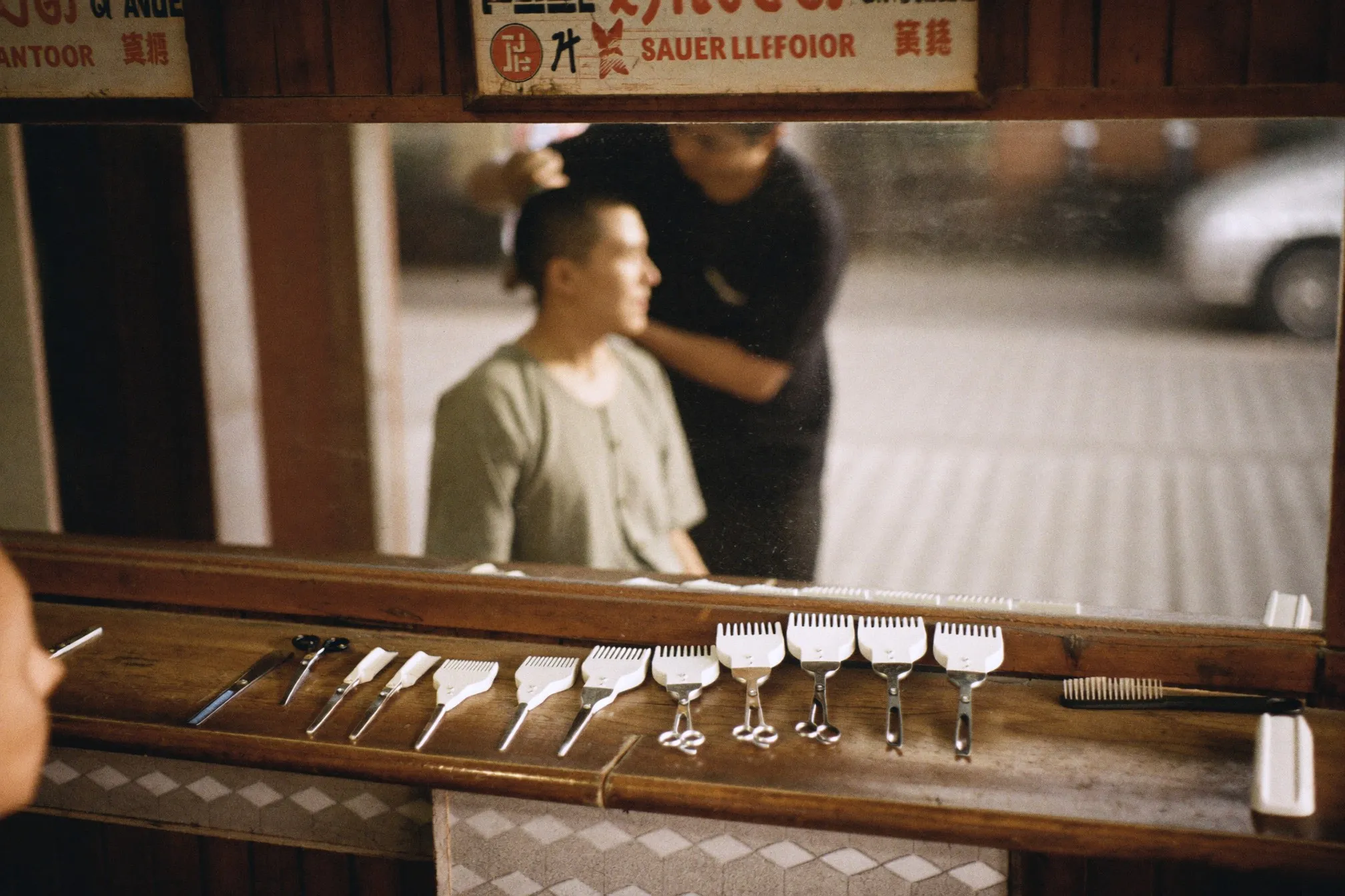 Barber's counter with clippers, guards and combs laid out while a man gets his hair cut in a Kuala Lumpur barbershop