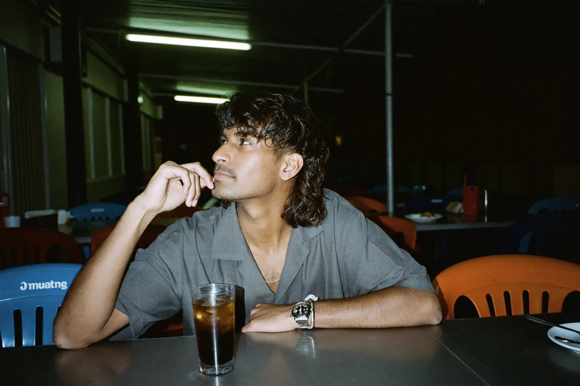 Indian Malaysian man with a wavy textured mullet sitting at a mamak table at night