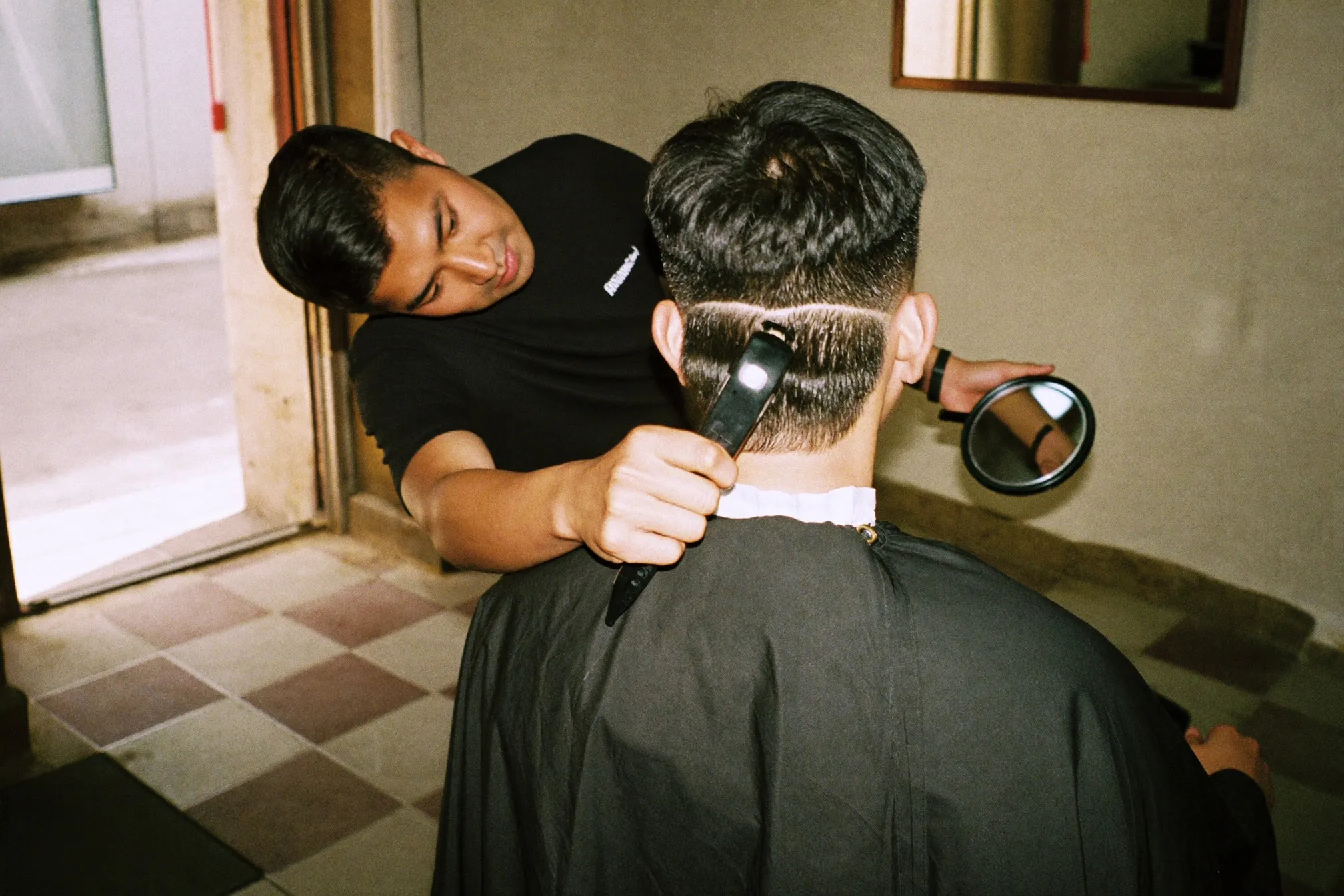 Barber holding a hand mirror behind a young Malay man to show the tapered back of his freshly cut modern mullet in a Kuala Lumpur barbershop