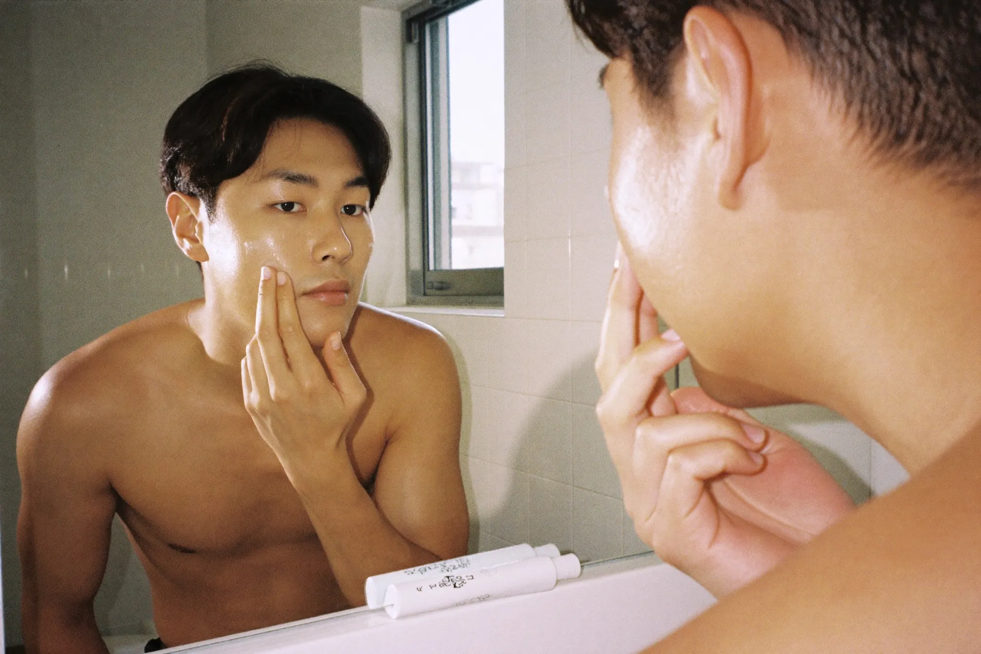 Man applying gel moisturiser to his face at a bathroom mirror in the morning