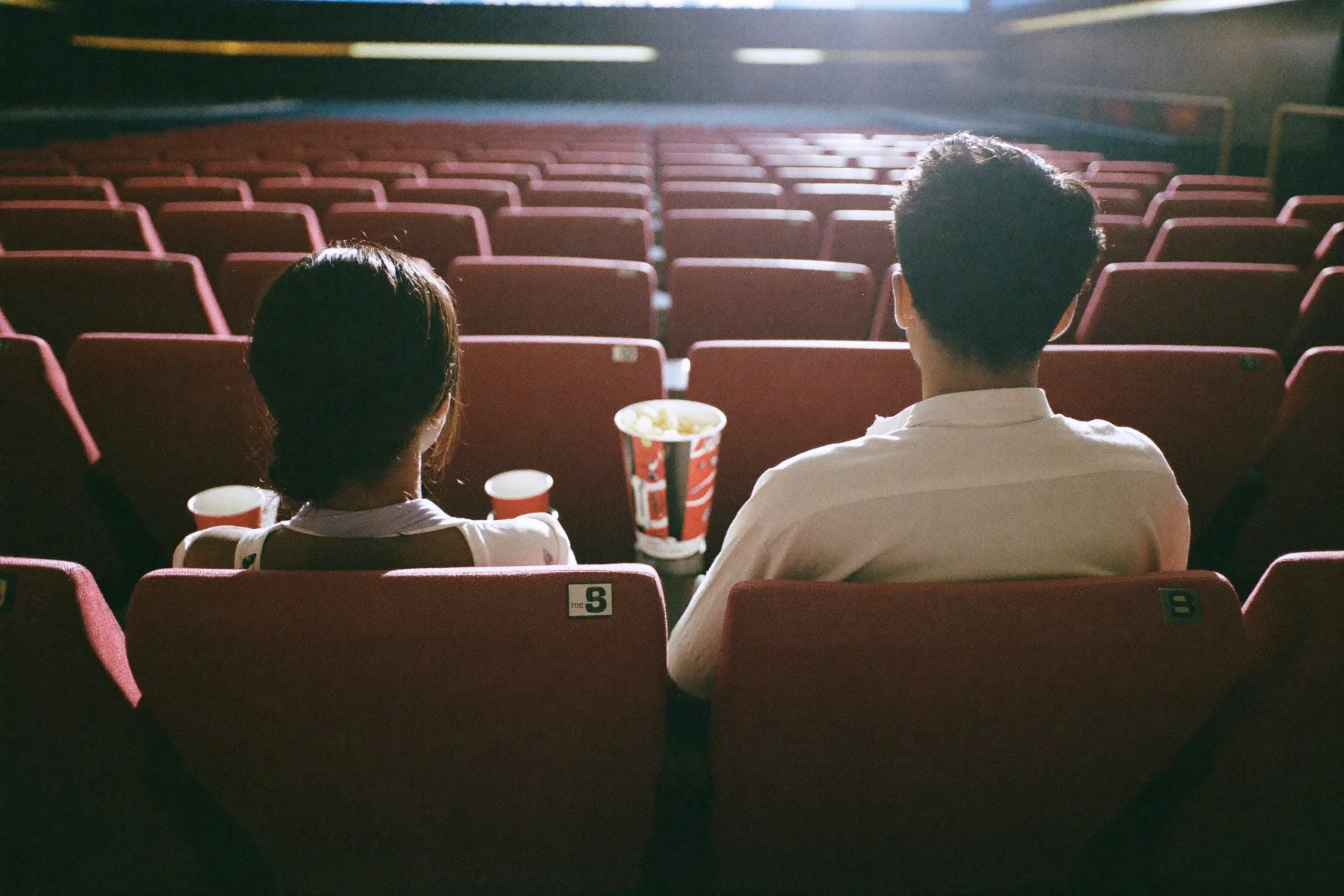 Couple seen from behind in a near-empty afternoon cinema with a tub of popcorn between their seats