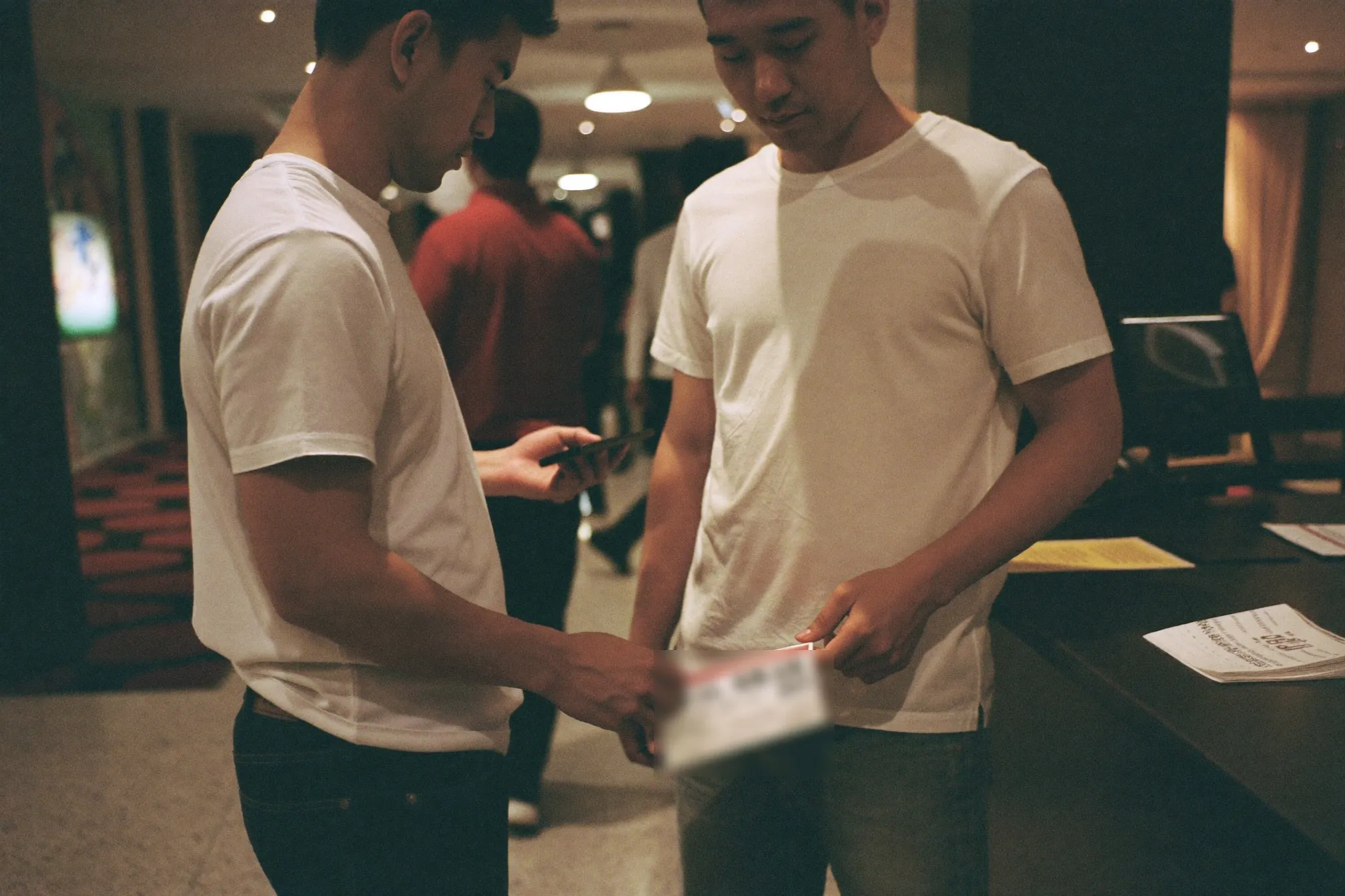 Cinema foyer at night in Kuala Lumpur with two men queueing at a ticket counter under warm overhead lighting