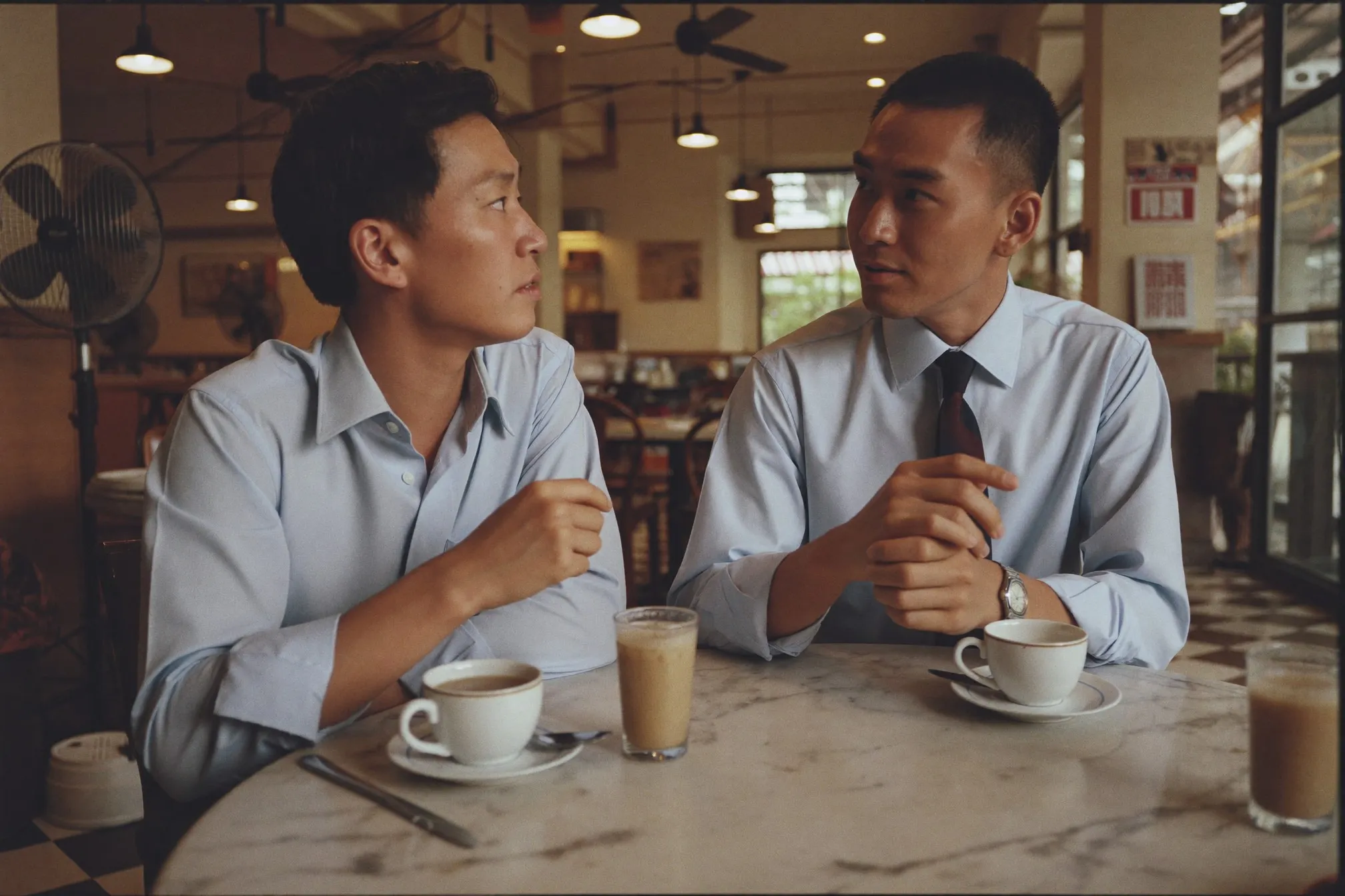 Two colleagues in office wear talking over teh tarik at a kopitiam table during lunch