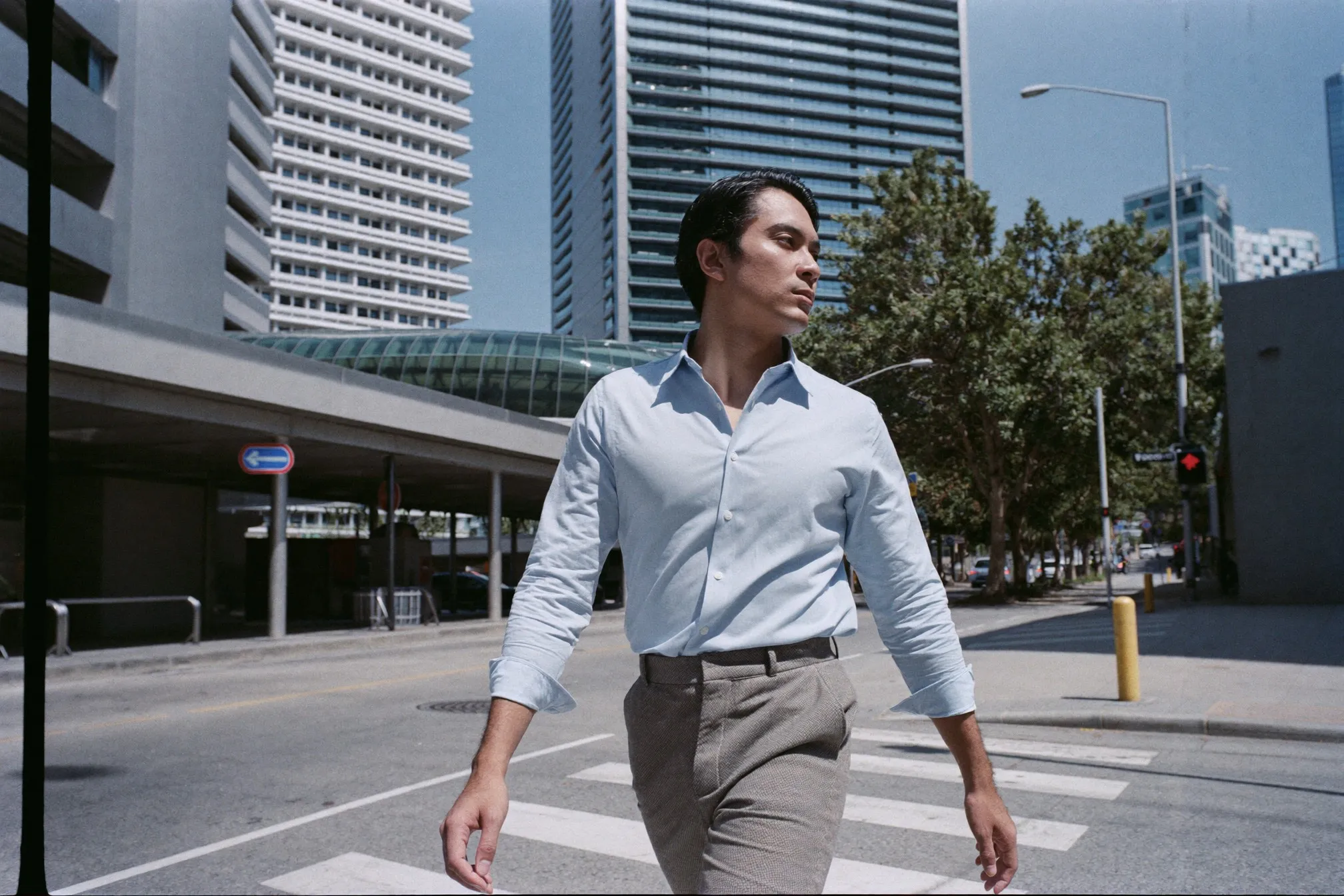 Man in a light blue shirt and grey trousers crossing a sunlit street in Singapore's central business district