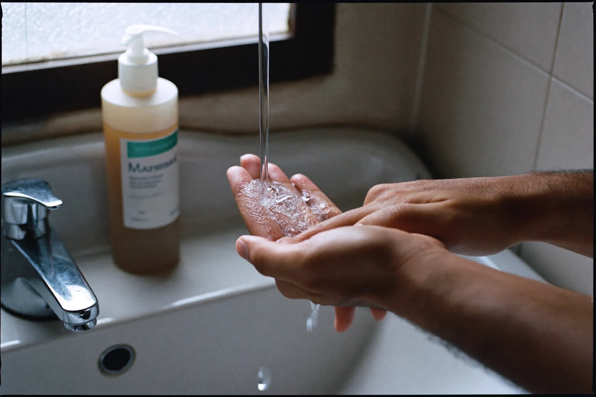 Close view of a gel cleanser lathering in a man's hands over a bathroom sink