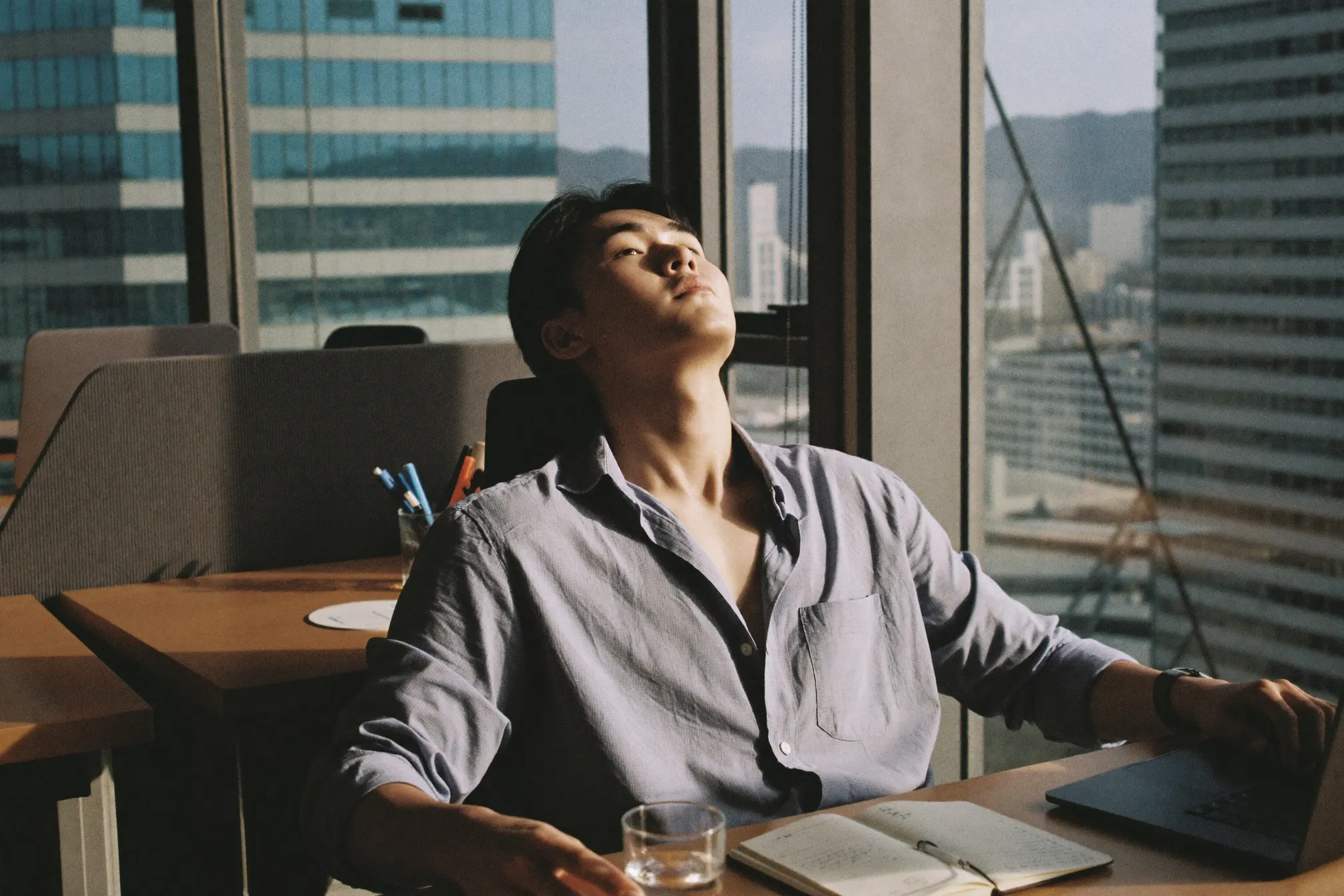 Man at an office desk beside a window with visible shine across his forehead in the afternoon