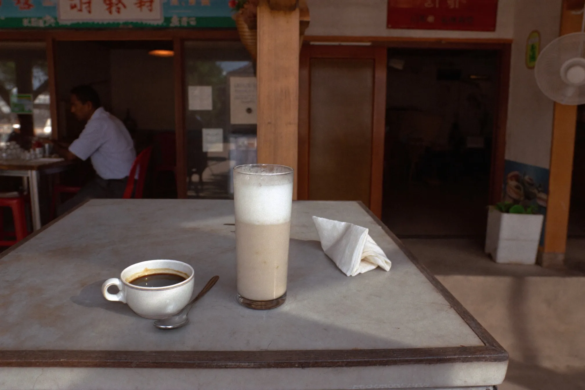 Glass of teh tarik and a mug of black coffee on a kopitiam table in the morning