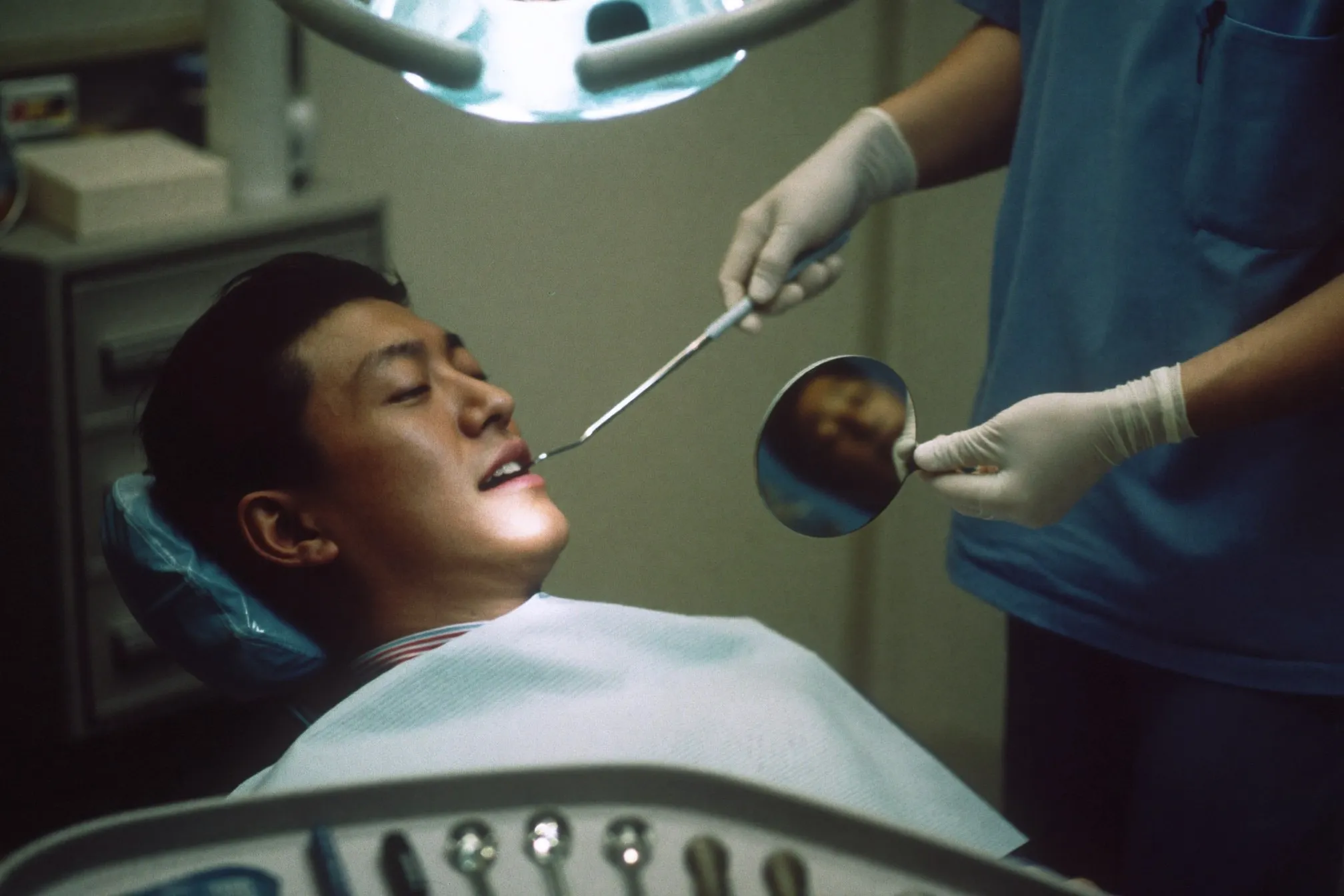 Man in a dental chair during a check-up under an overhead examination lamp