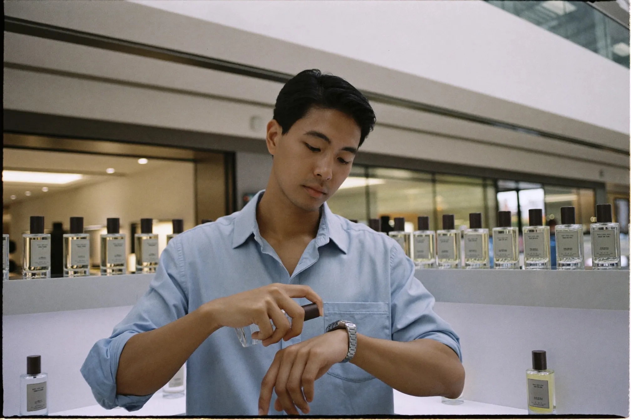 Man in a shirt testing perfume on his wrist at a bright fragrance counter in a Kuala Lumpur mall