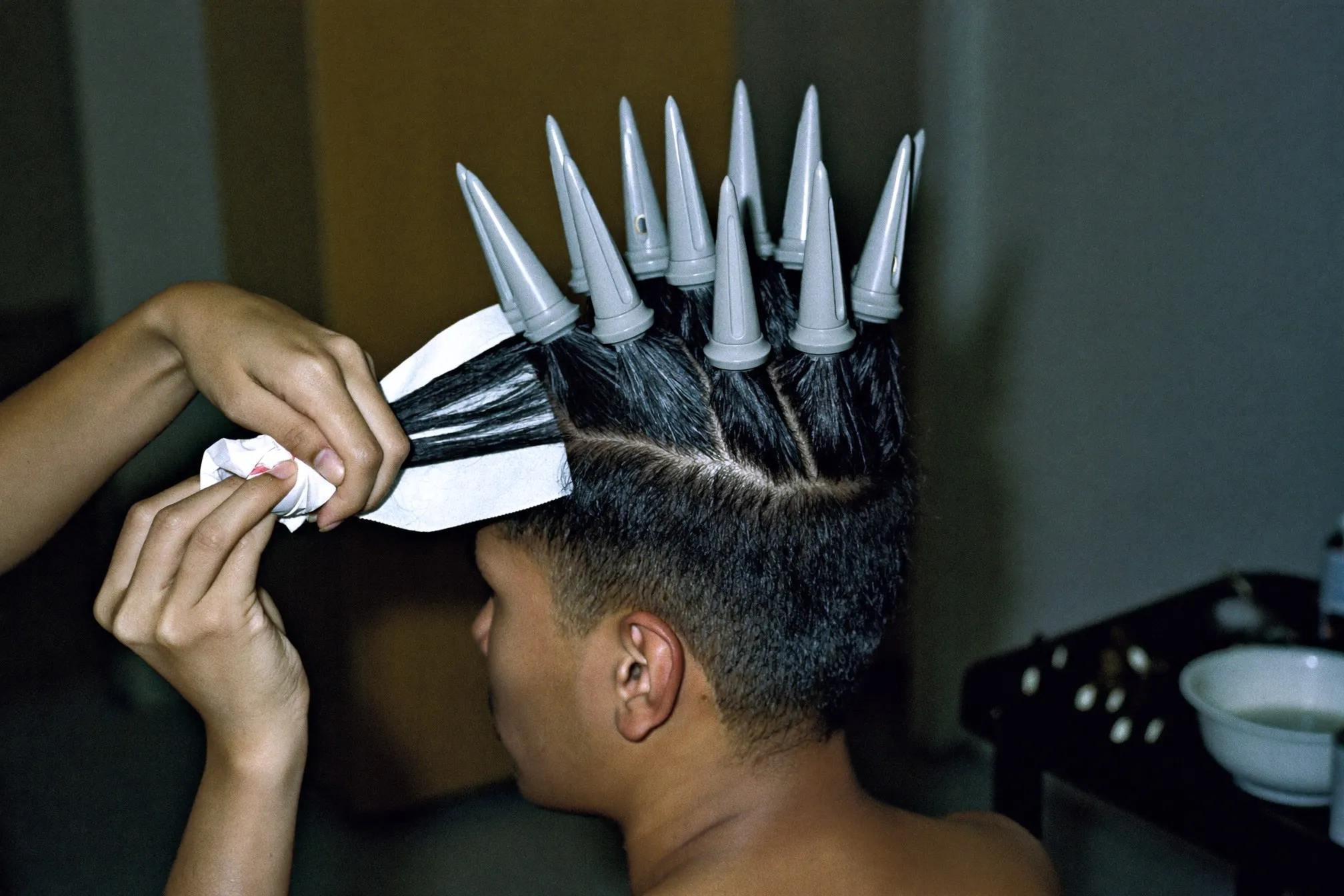 Stylist winding a section of a man's hair onto a perm rod at a small Singapore salon